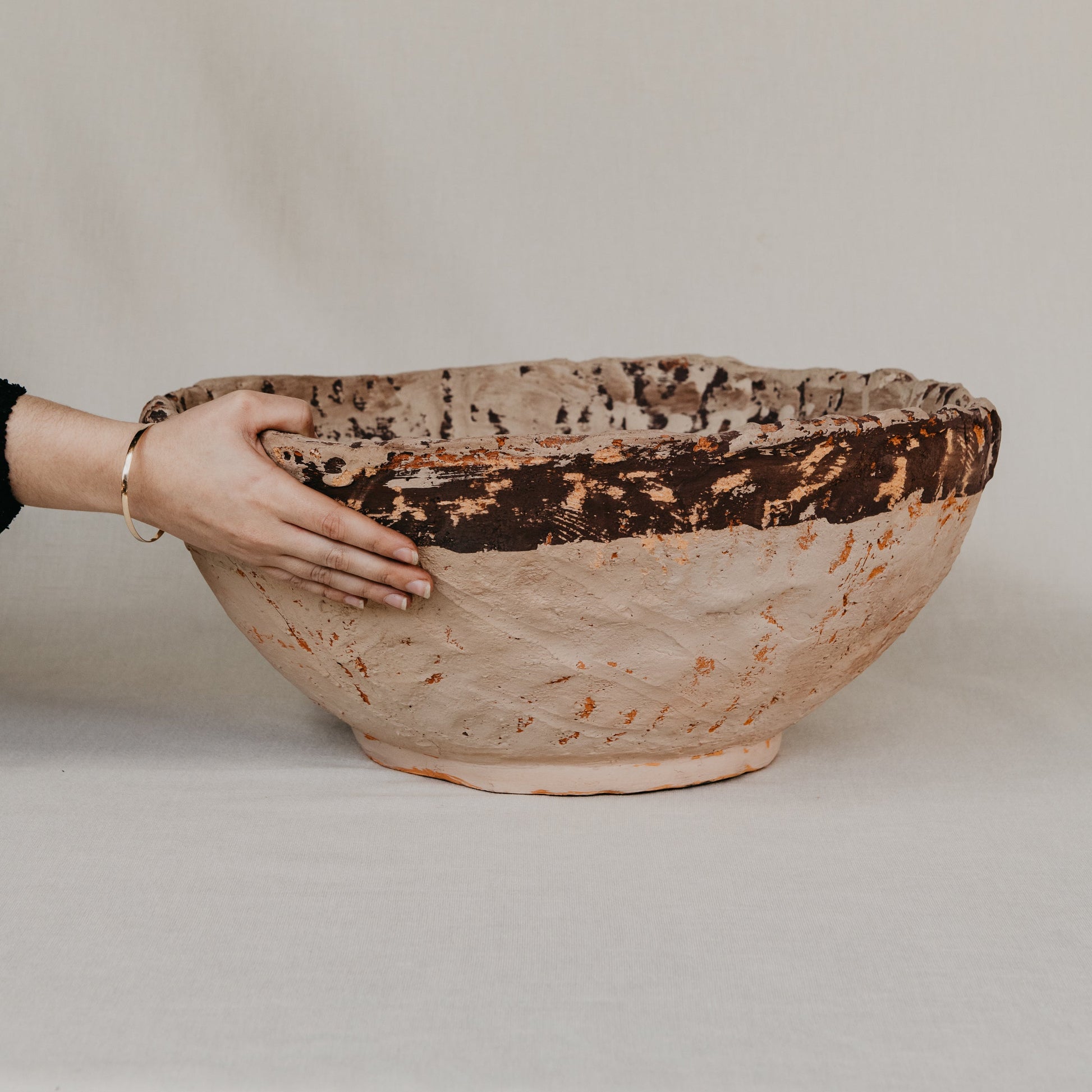Hand holding a large ceramic bowl with a textured surface on a plain background