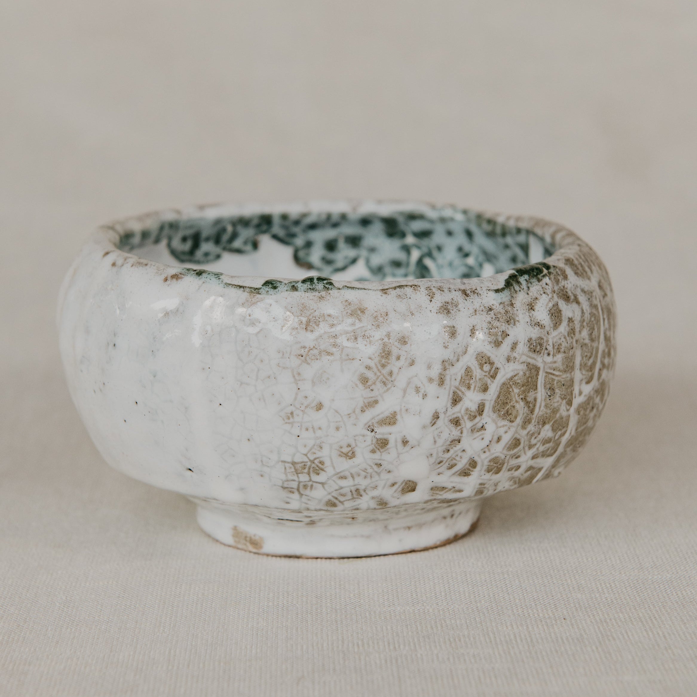 Small ceramic bowl with textured surface and green interior on a beige background