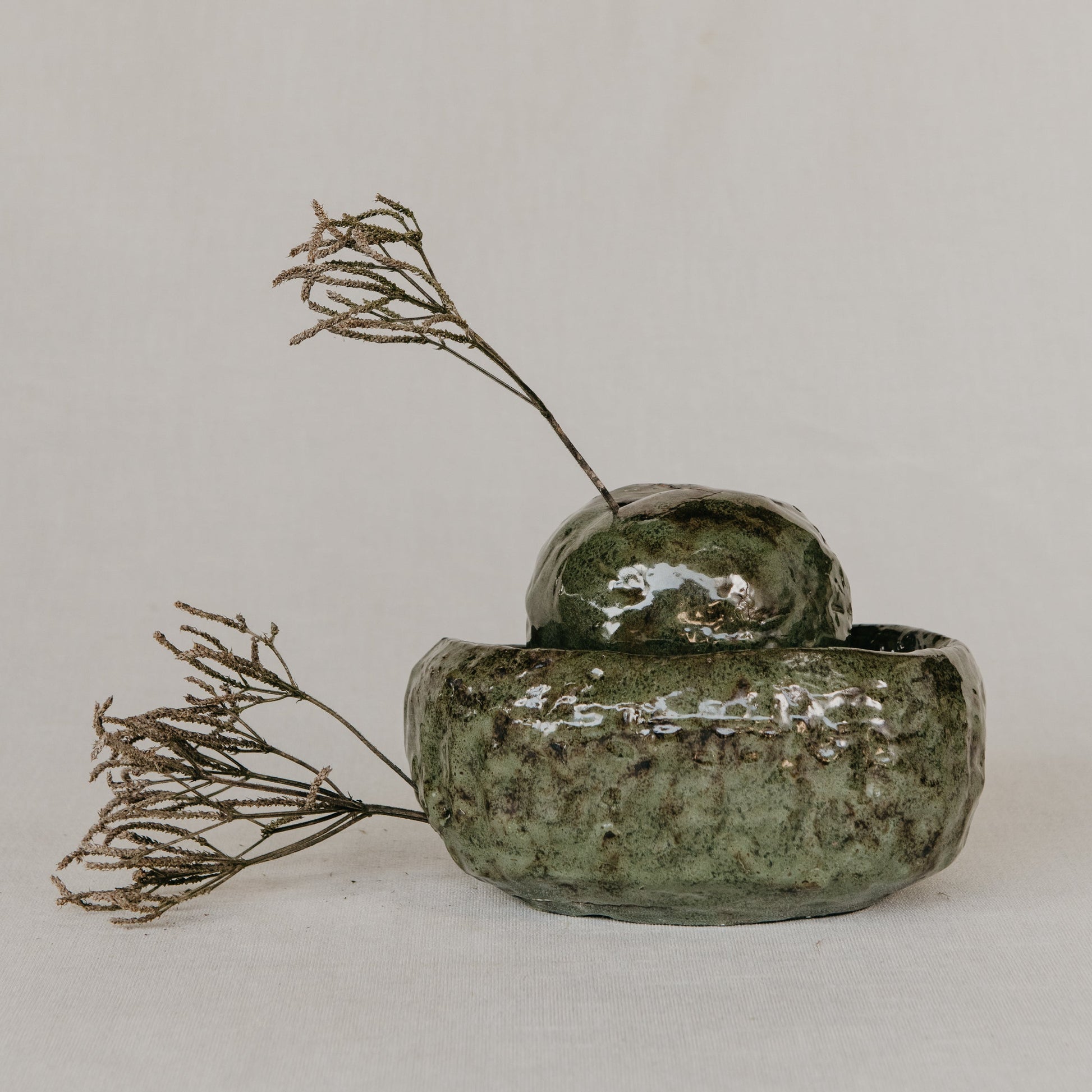 Green ceramic container with dried plants on a light gray background