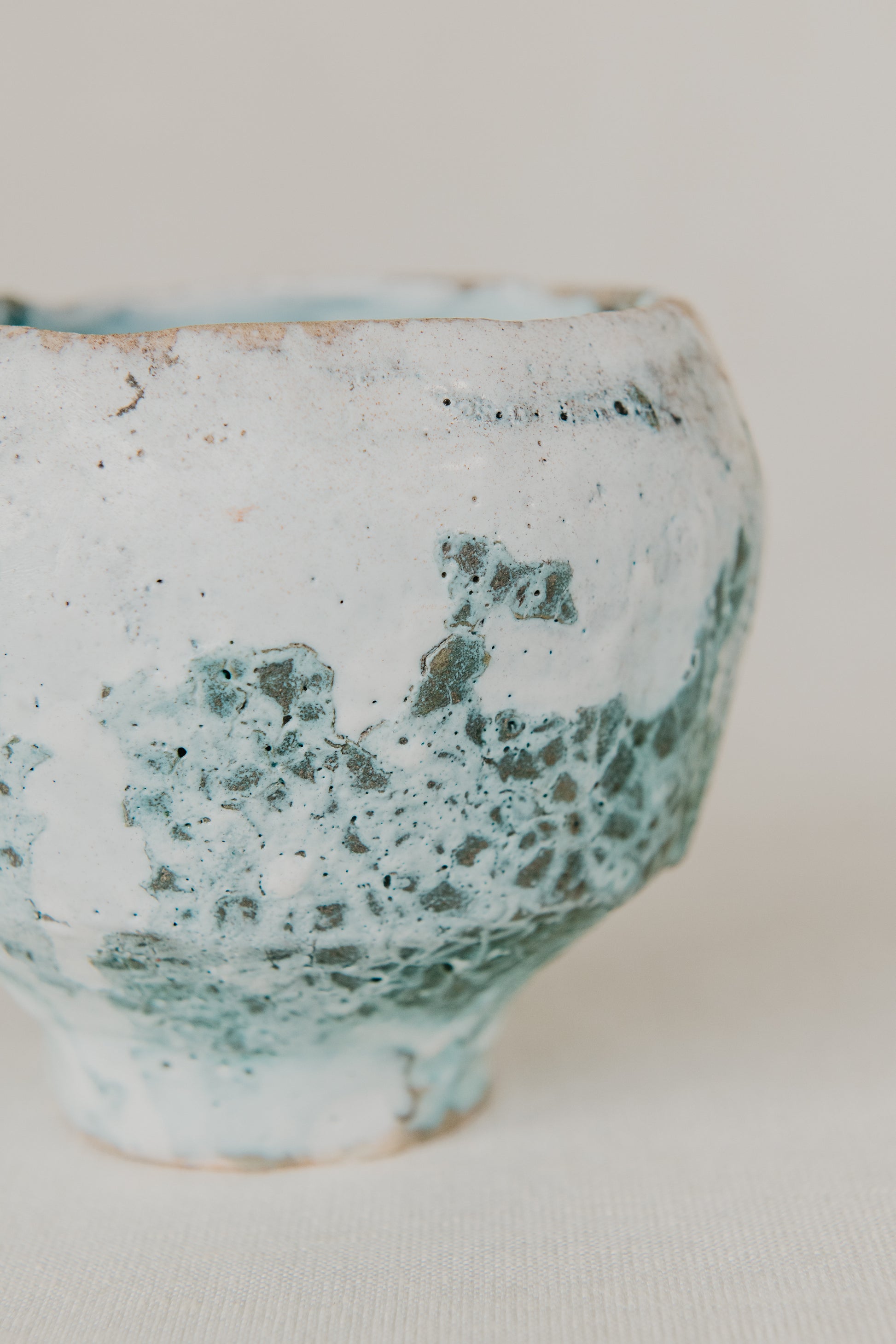 Ceramic cup with green and white speckled glaze on a plain background