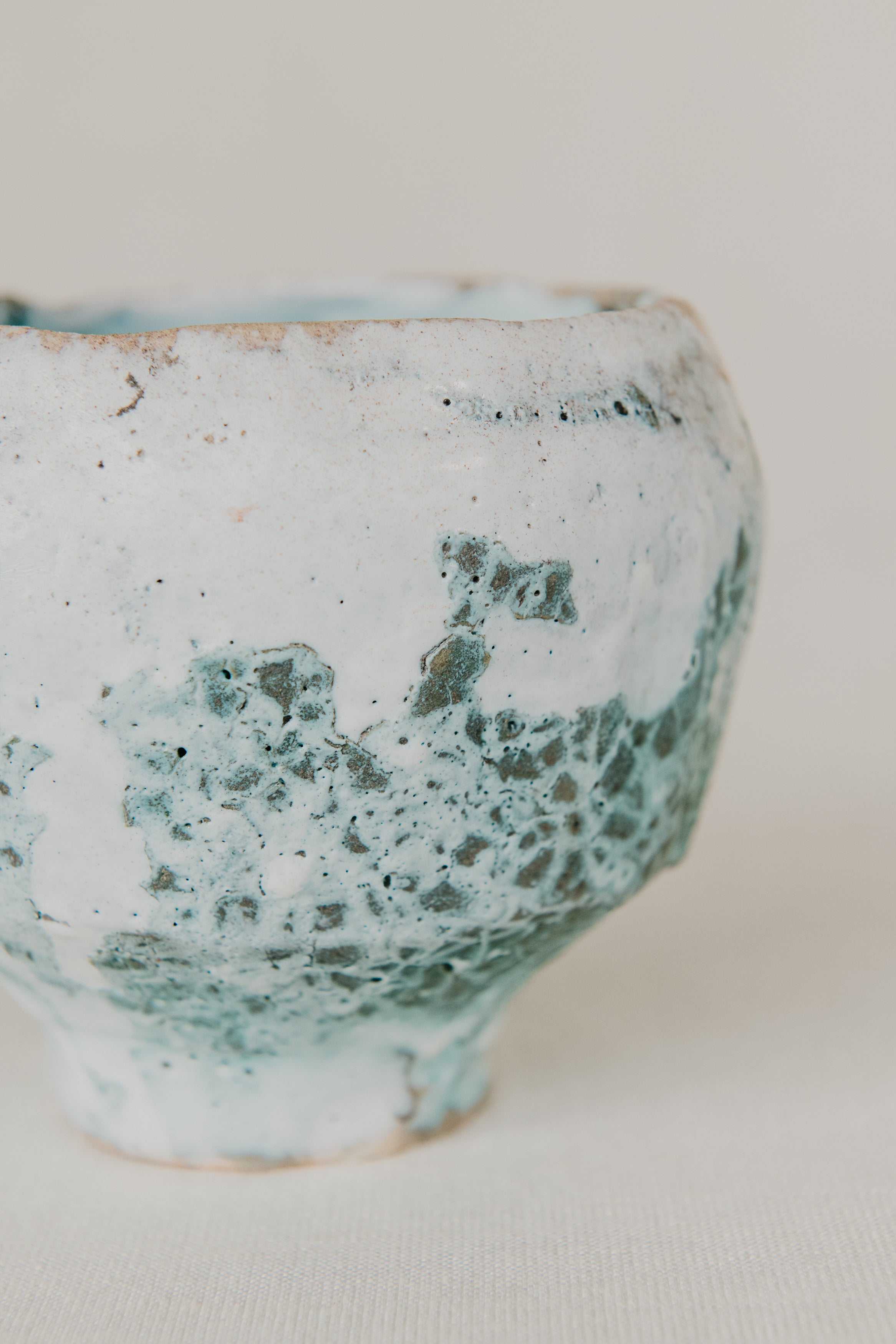 Ceramic cup with green and white speckled glaze on a plain background