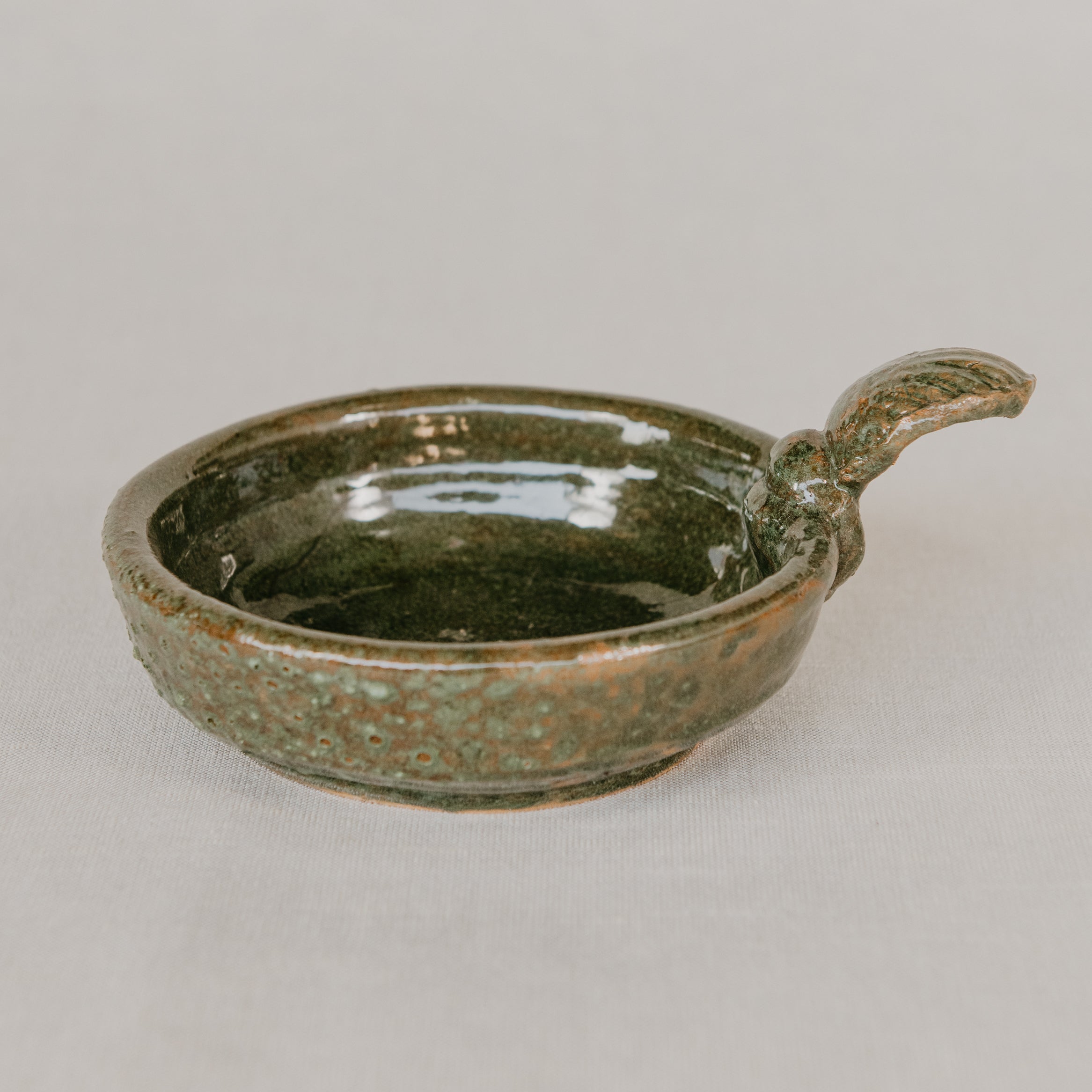 Green ceramic dish with handle on a light gray background