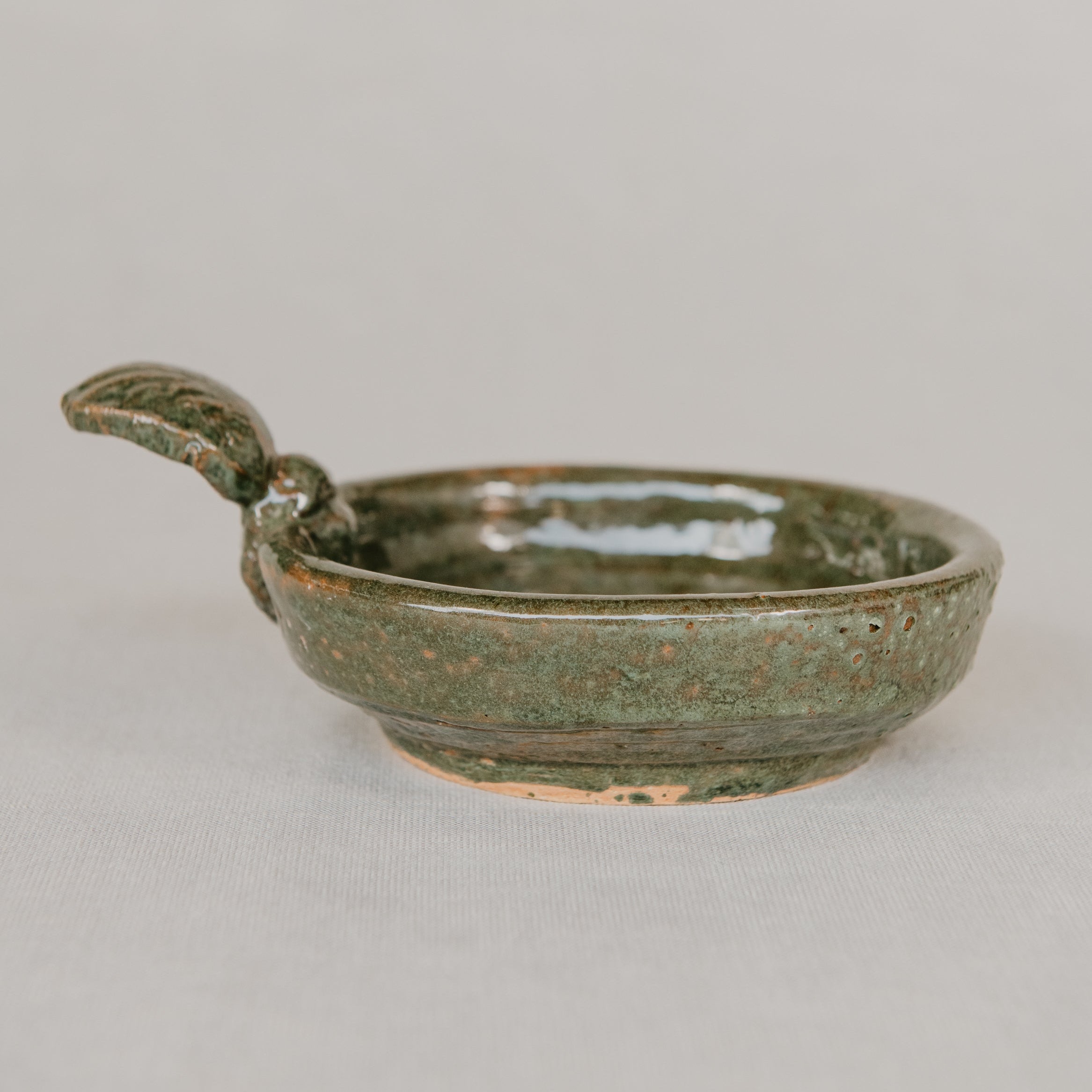 Green ceramic dish with handle on a light gray background