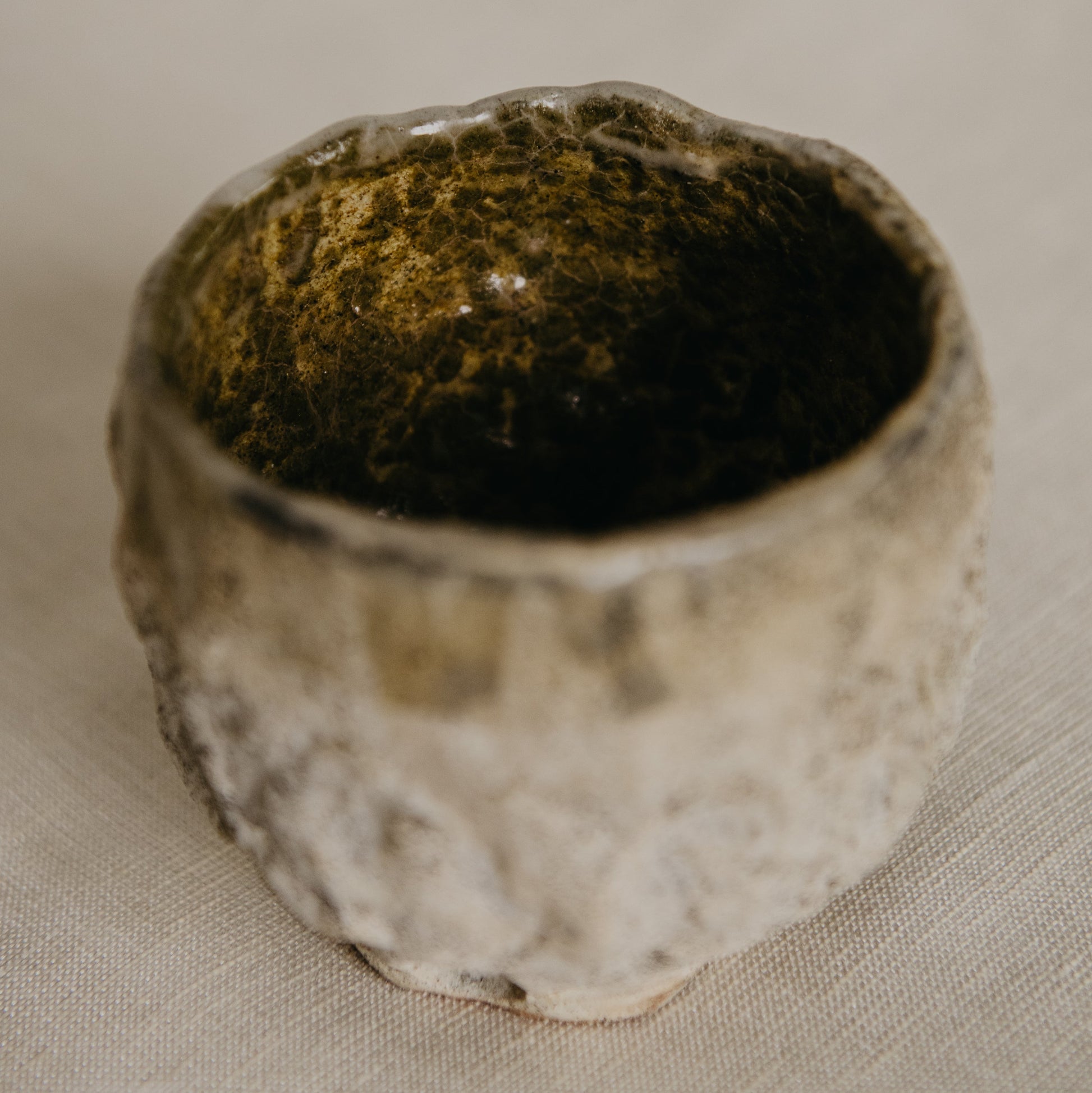 Small ceramic cup with textured surface on a beige fabric background