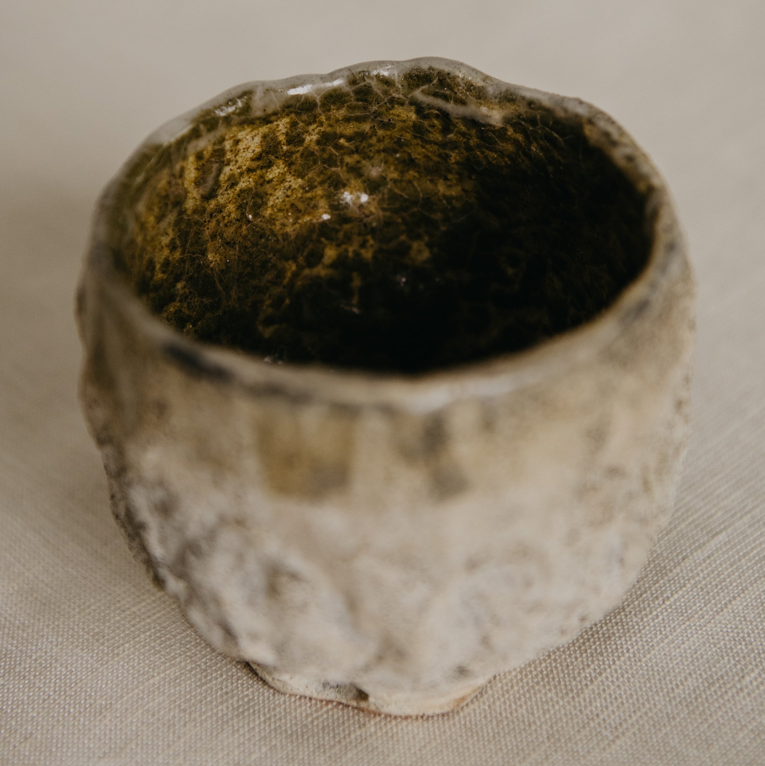 Small ceramic cup with textured surface on a beige fabric background