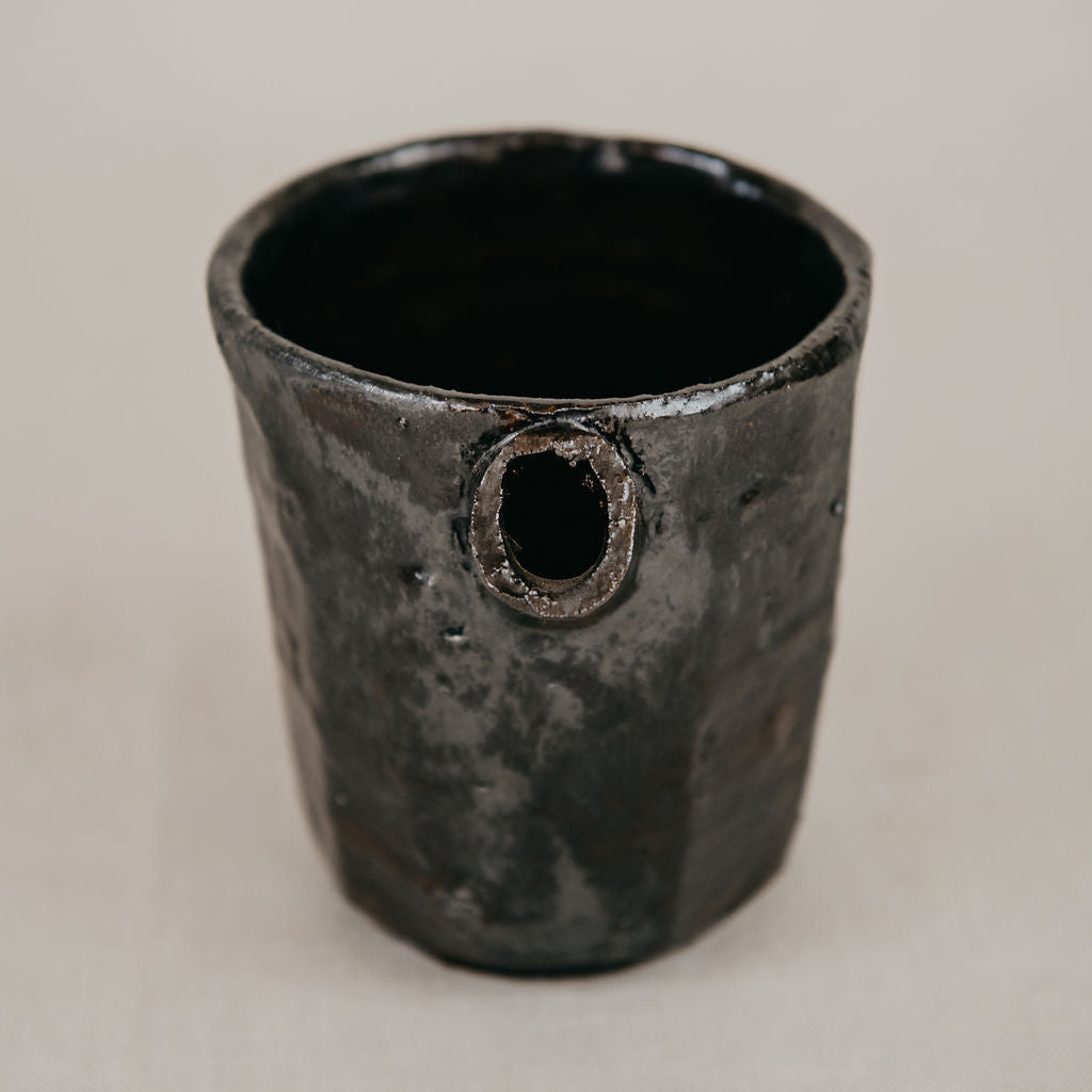 Black ceramic cup with a circular hole on a beige background
