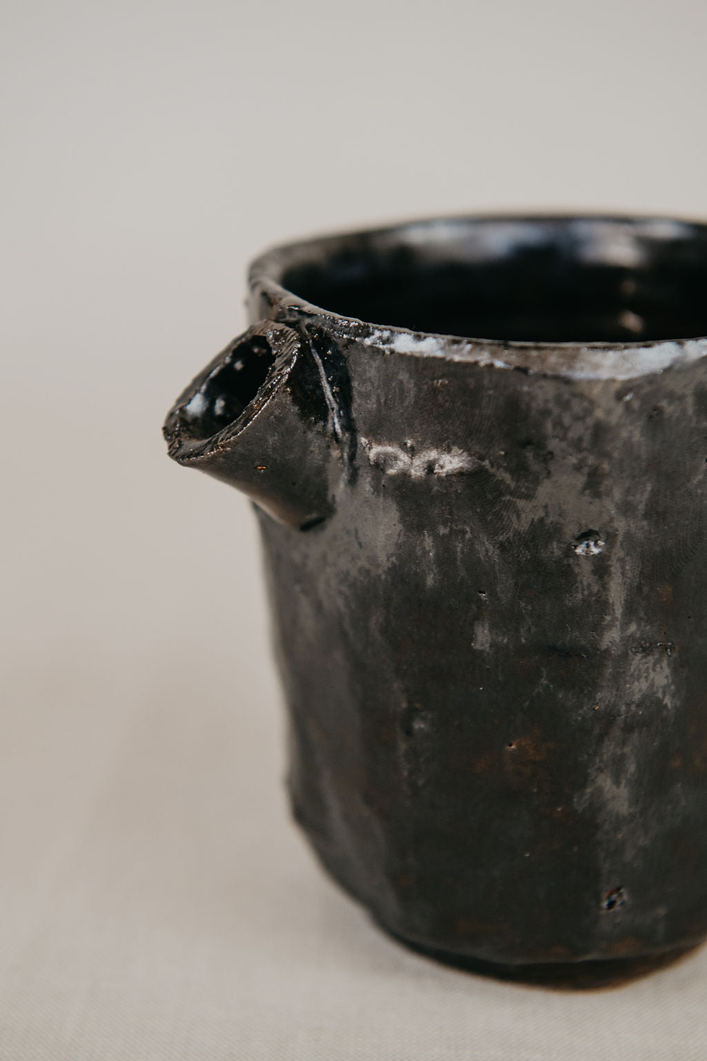 Black ceramic pot with a handle on a light gray background