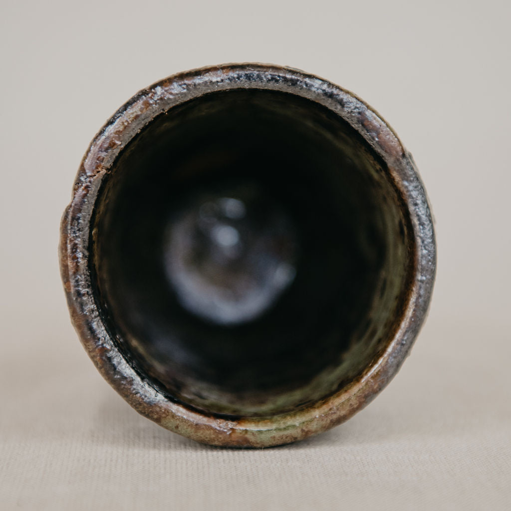 Cylindrical ceramic object with a textured rim on a beige background