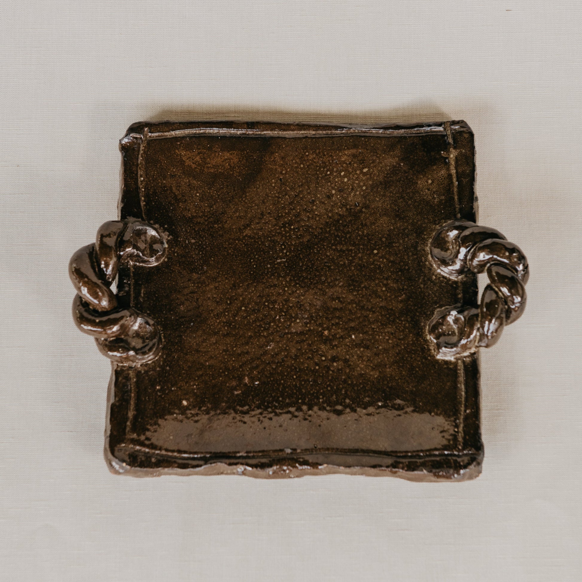 Brown ceramic platter with textured surface on a beige background