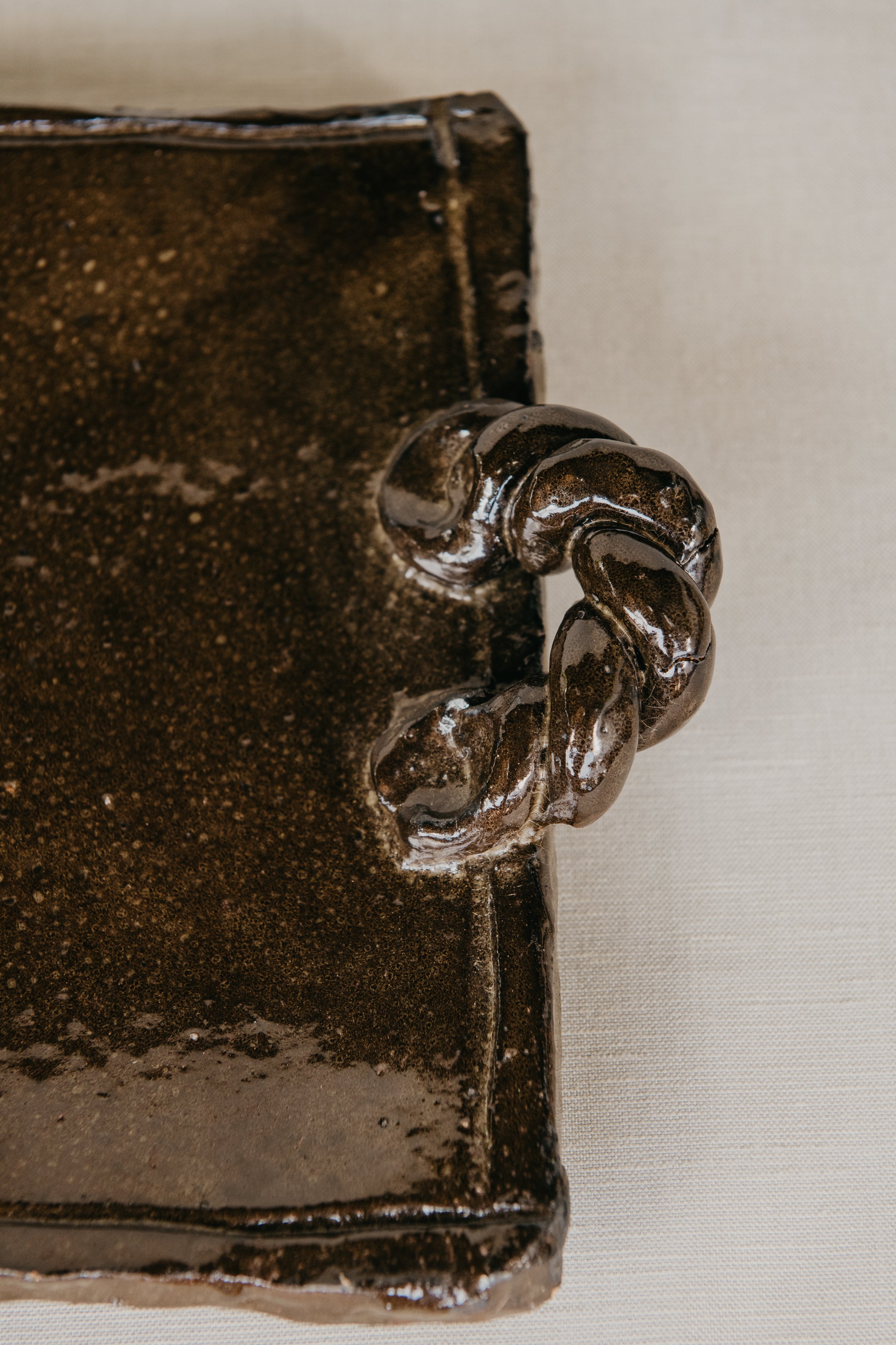 Brown ceramic platter with textured surface on a beige fabric background