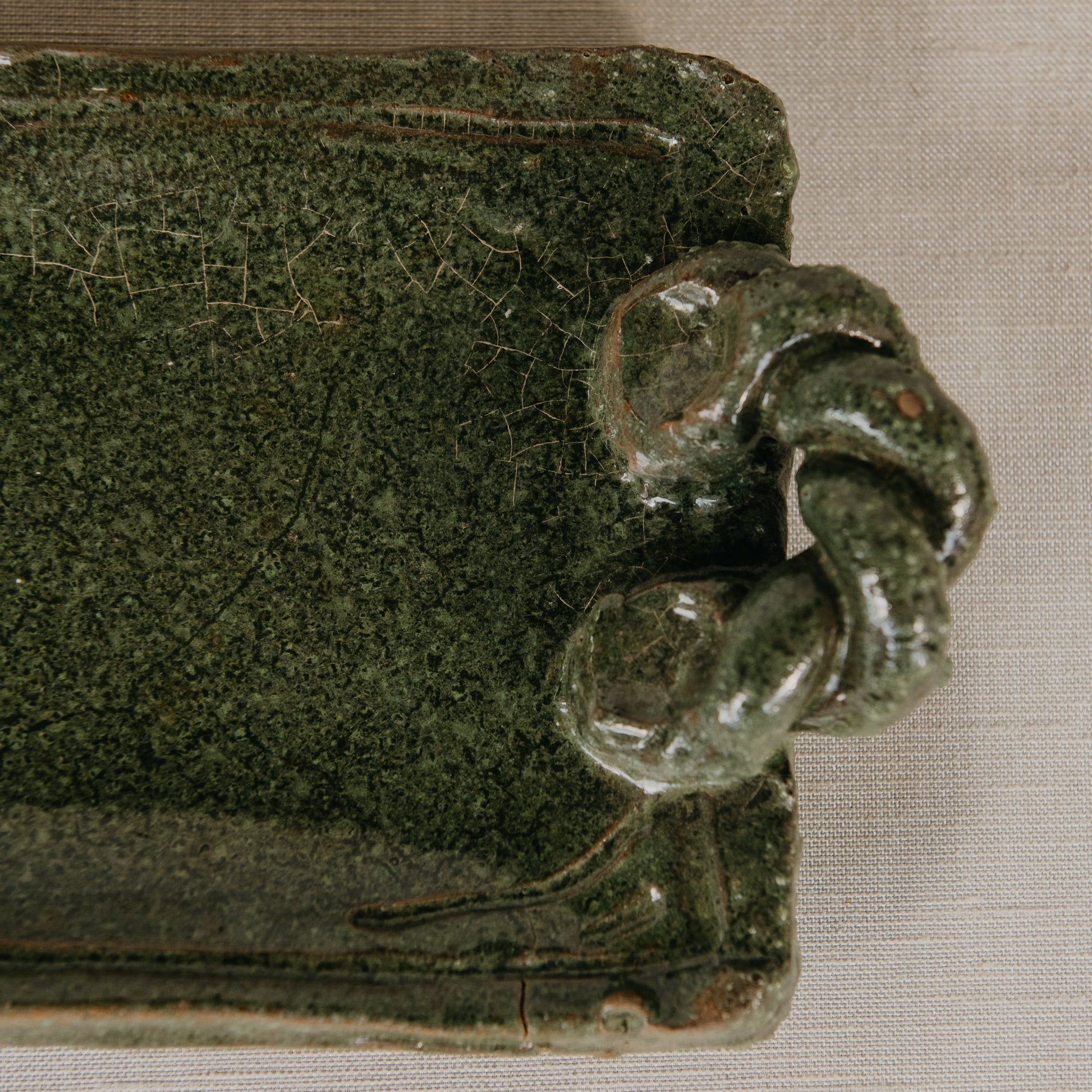 Green ceramic object with a decorative handle on a beige background