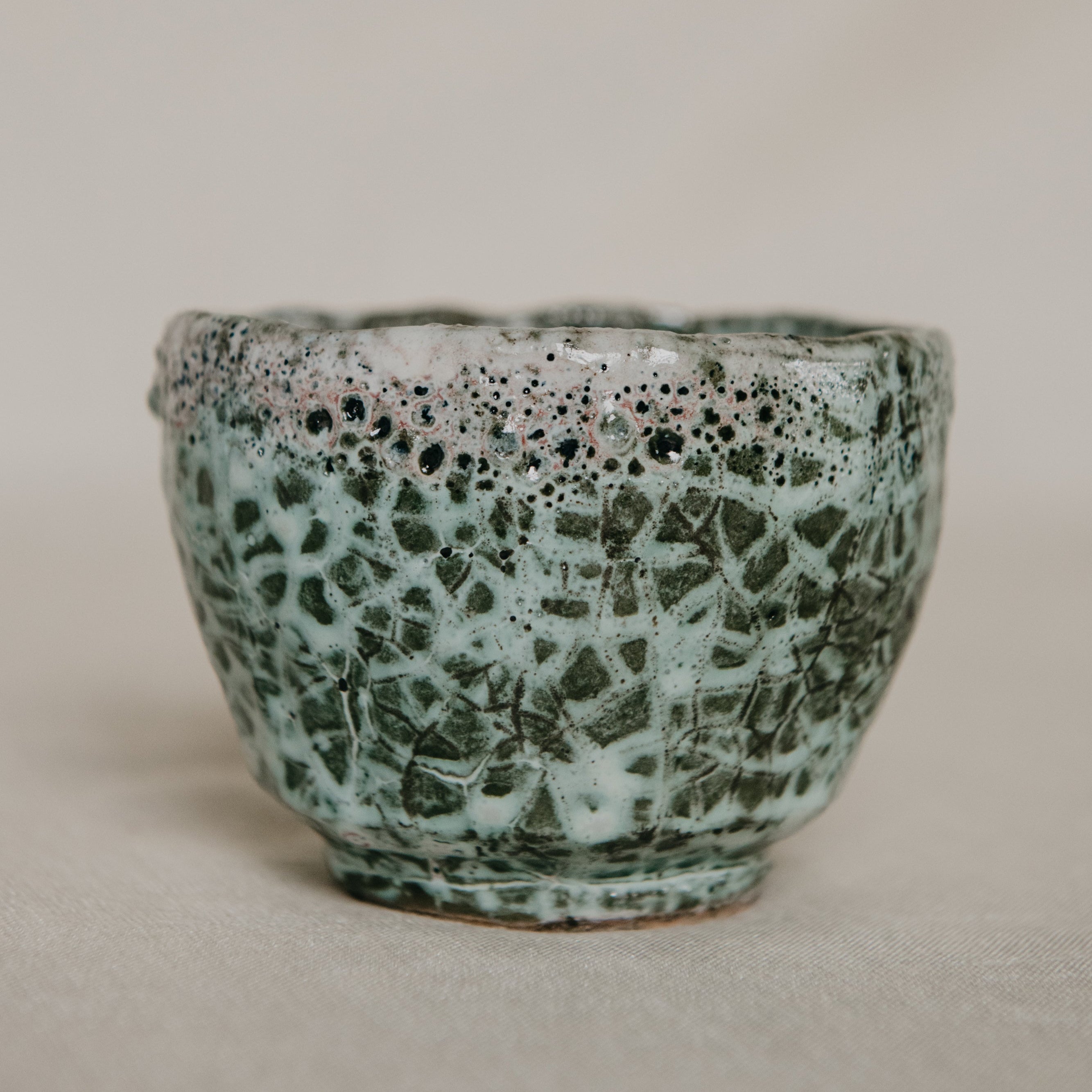 Ceramic cup with speckled green and brown glaze on a beige background