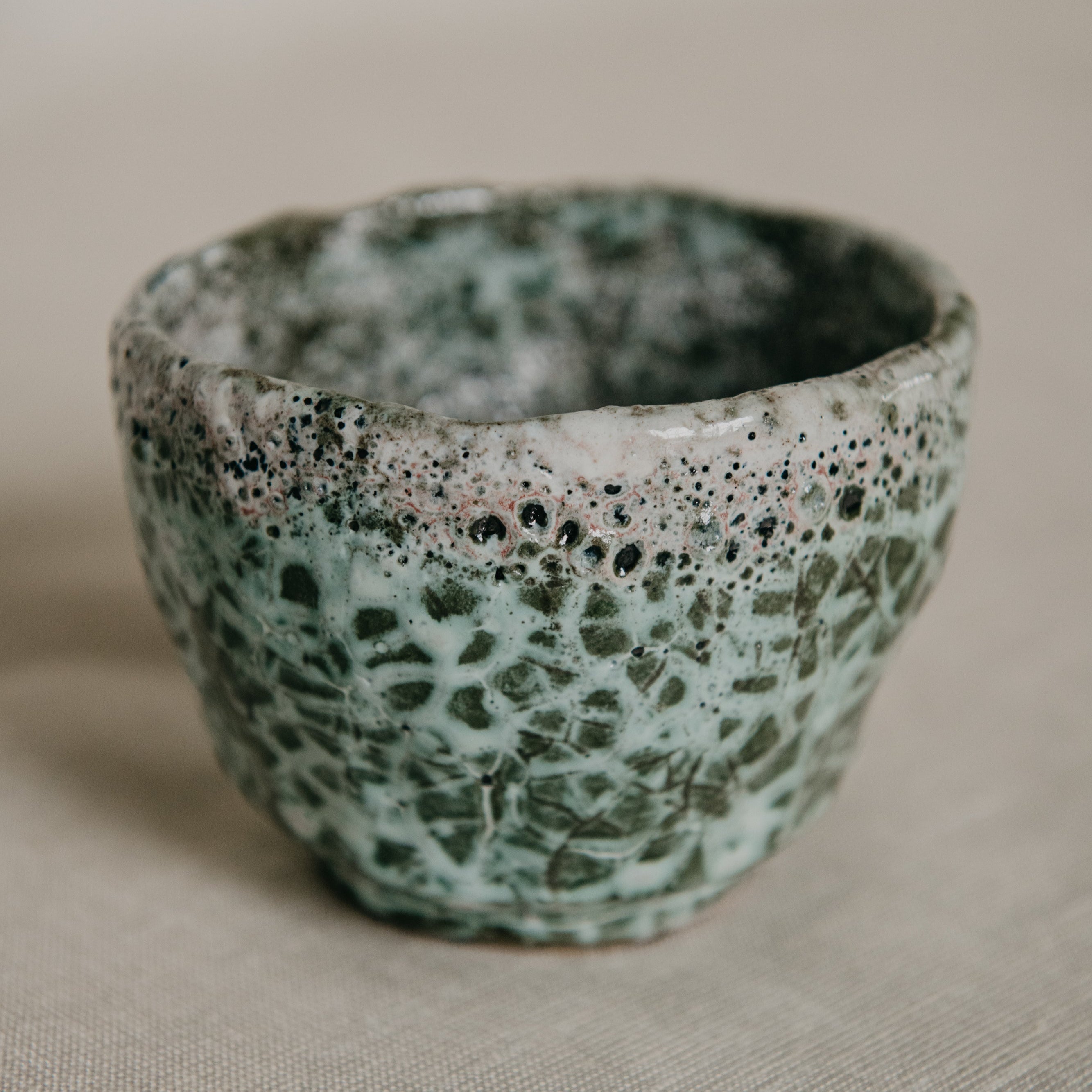 Speckled green and brown ceramic cup on a beige surface