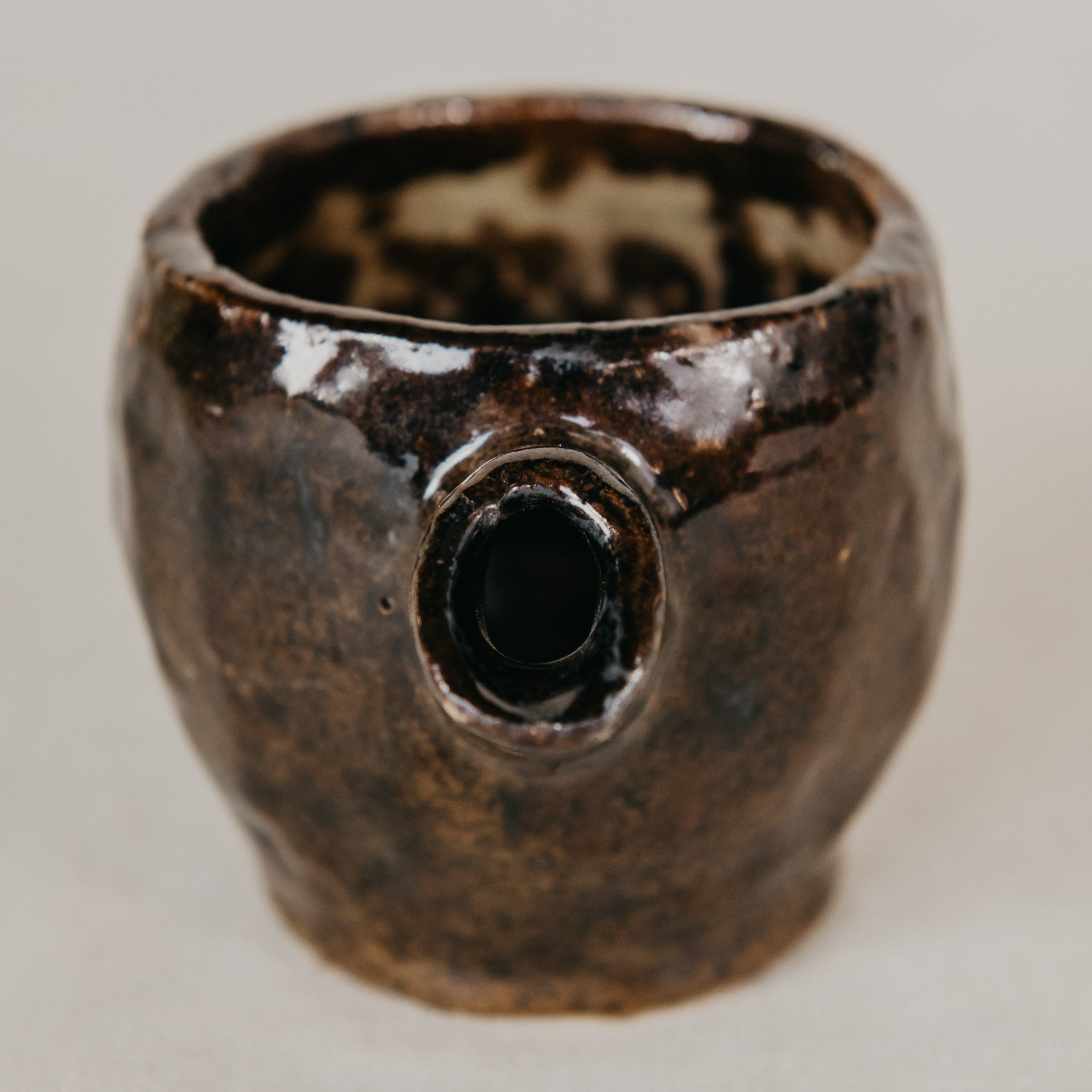 Brown ceramic cup with a unique design on a light gray background