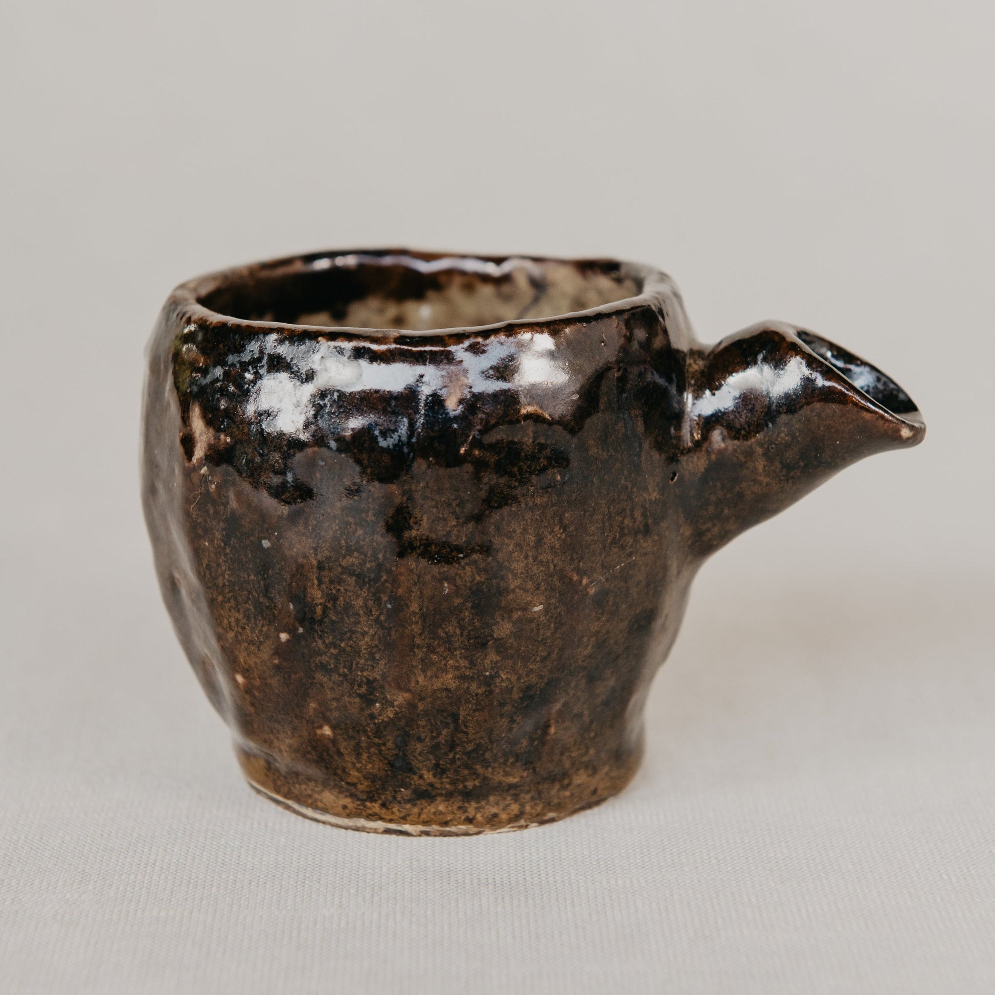 Small ceramic pitcher with a handle on a neutral background