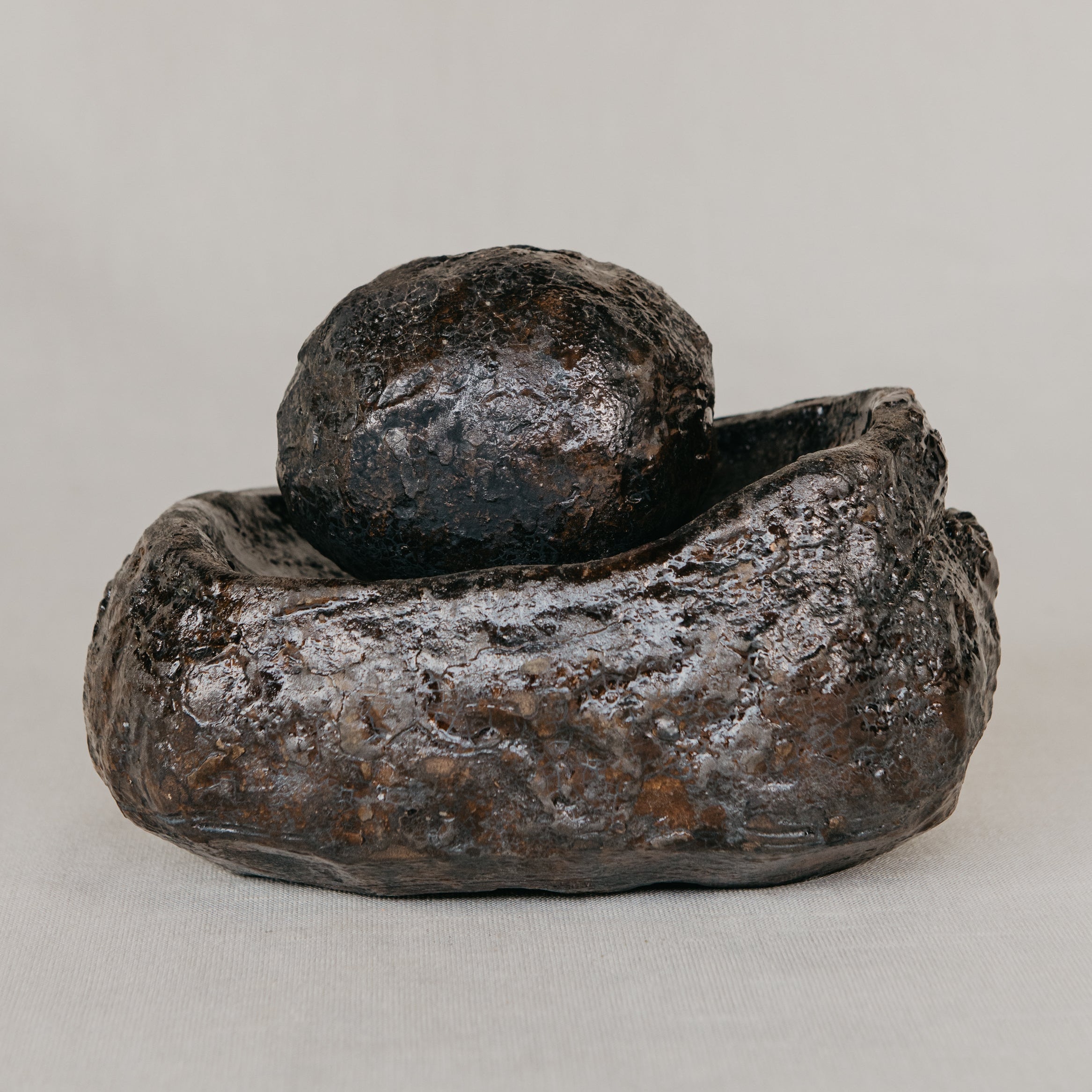 Rustic metal sculpture of a bowl and rock on a neutral background