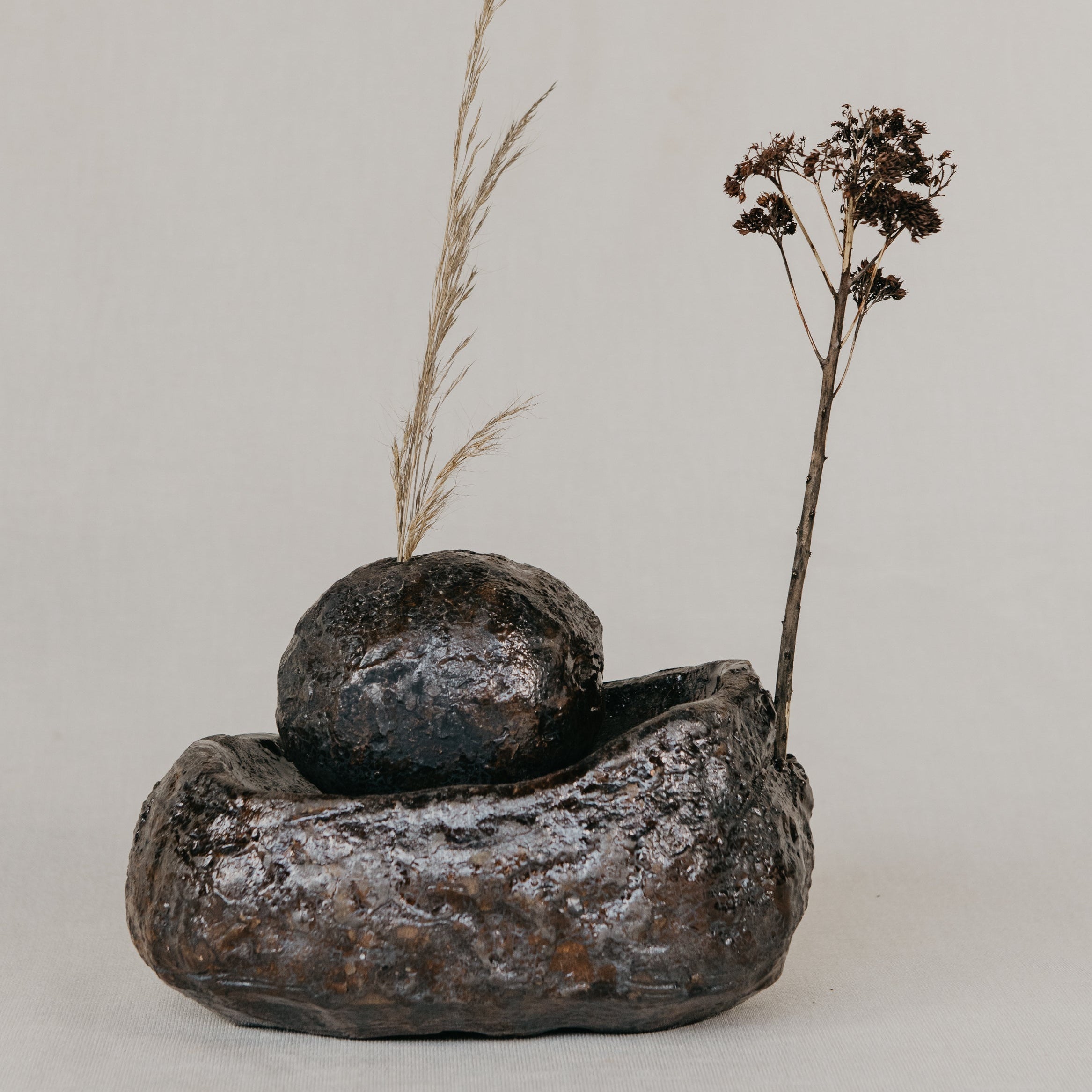 Decorative arrangement with textured stones and dried plants on a neutral background