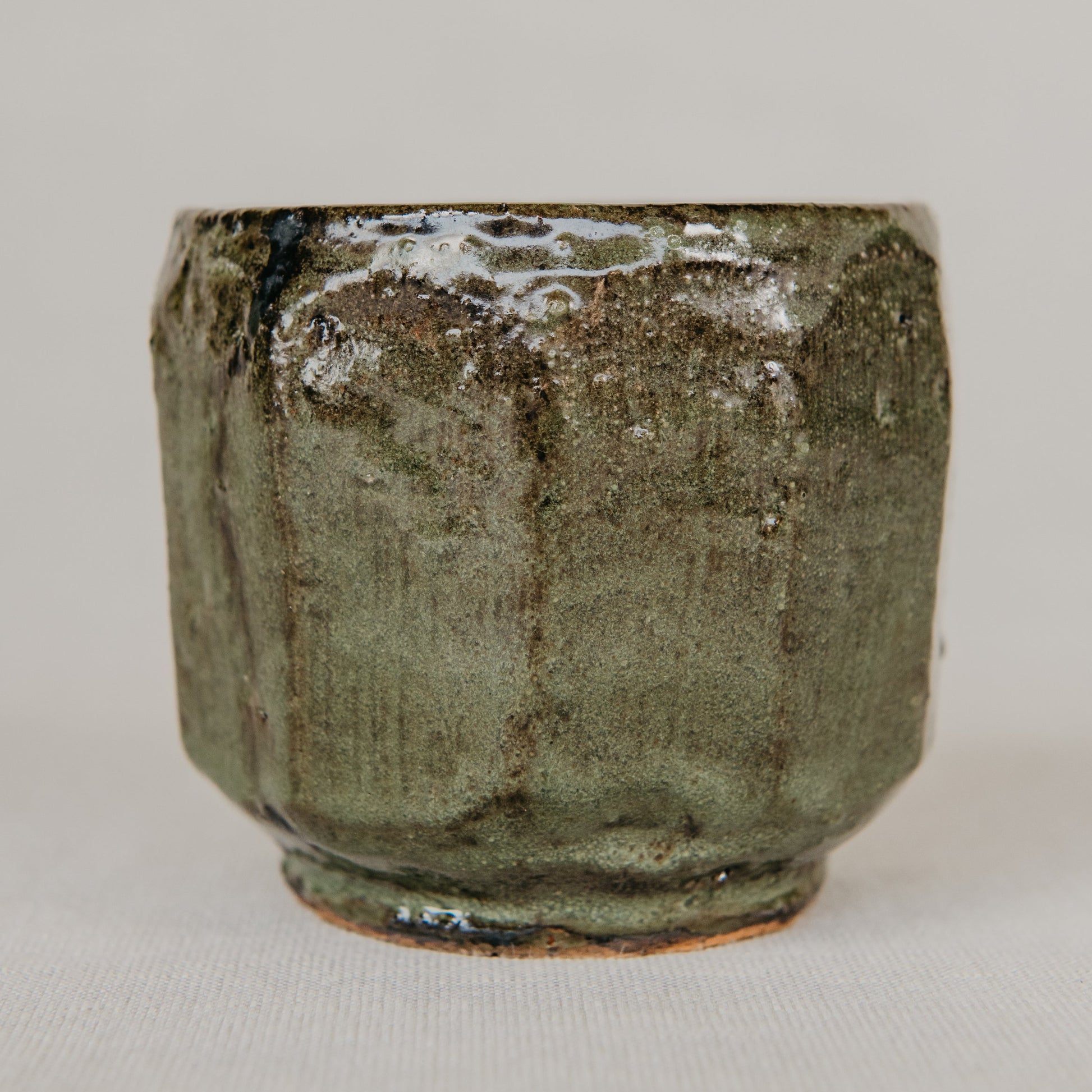 Green ceramic cup with textured surface on a light gray background