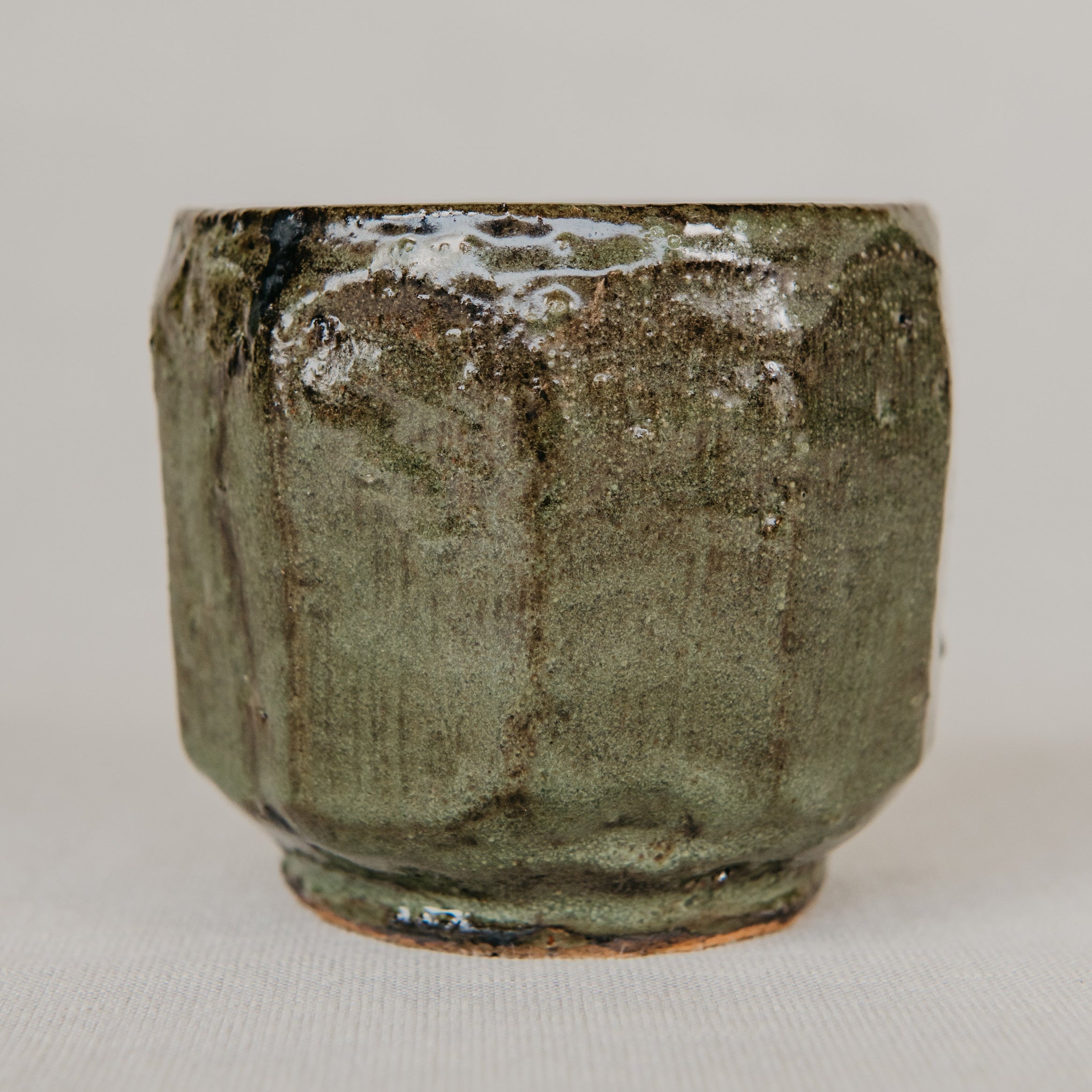 Green ceramic cup with textured surface on a light gray background