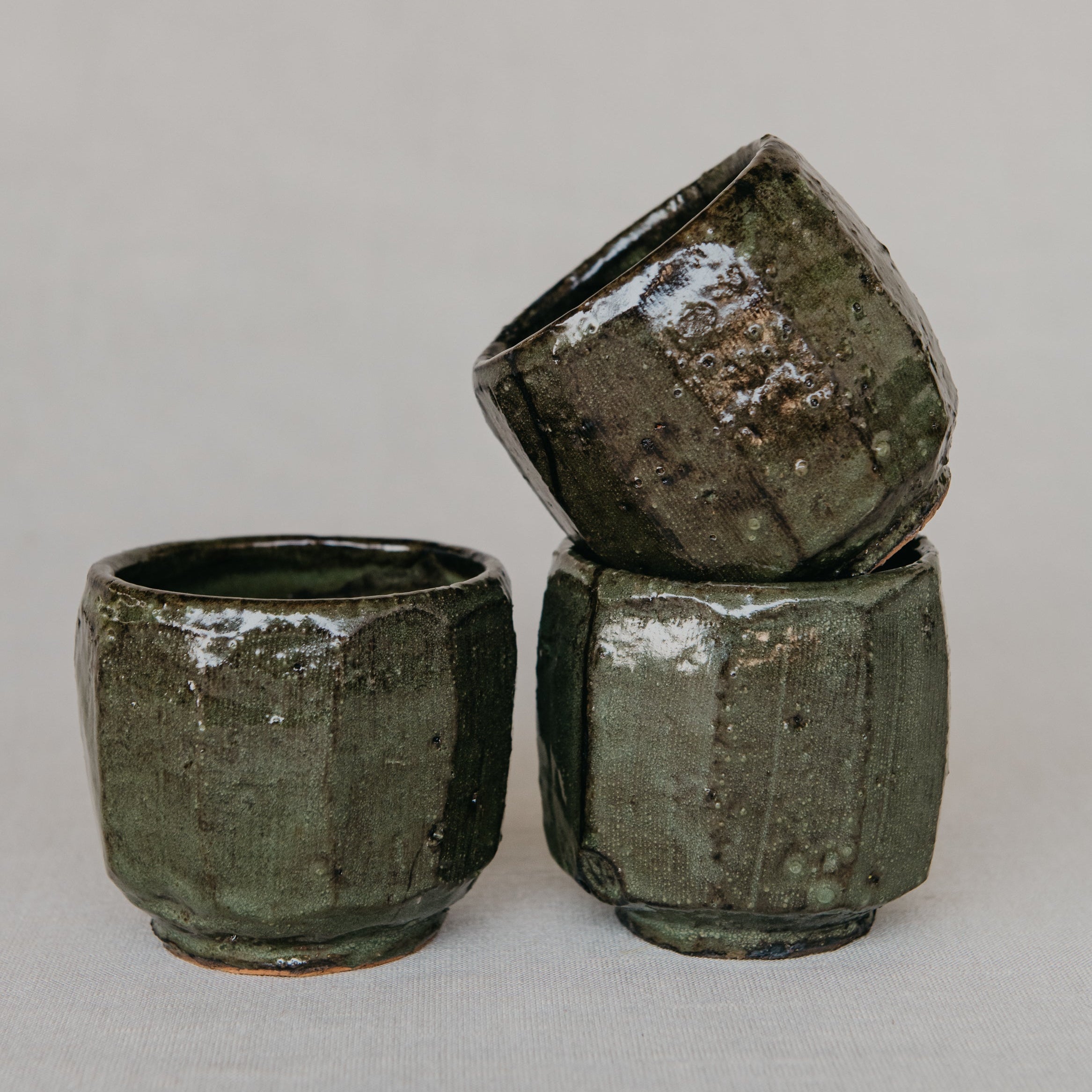 Three green ceramic cups of varying sizes on a light gray background