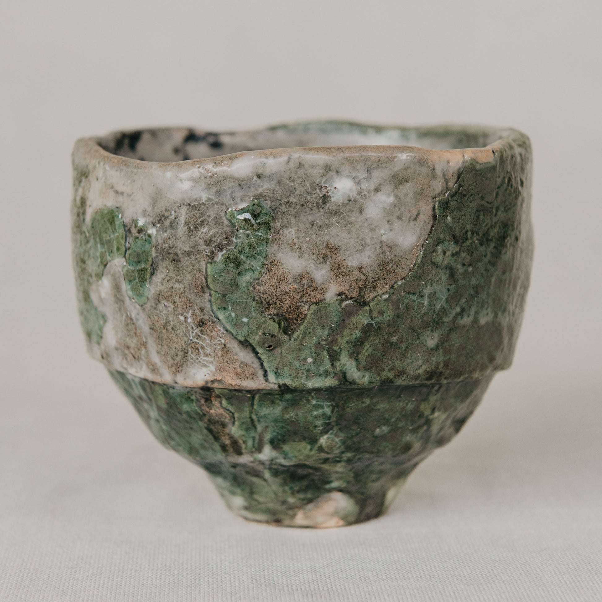 Vintage ceramic cup with green and brown patina on a light gray background