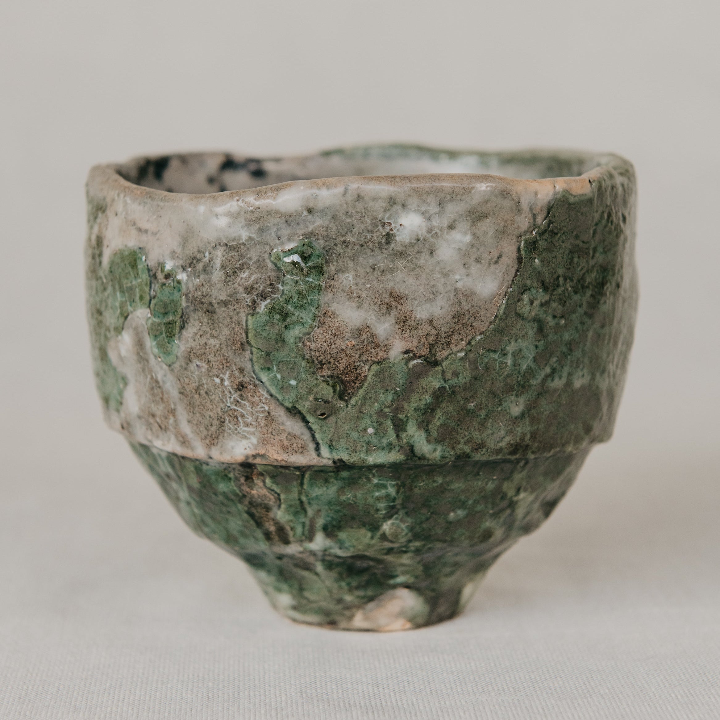 Vintage ceramic cup with green and brown patina on a light gray background