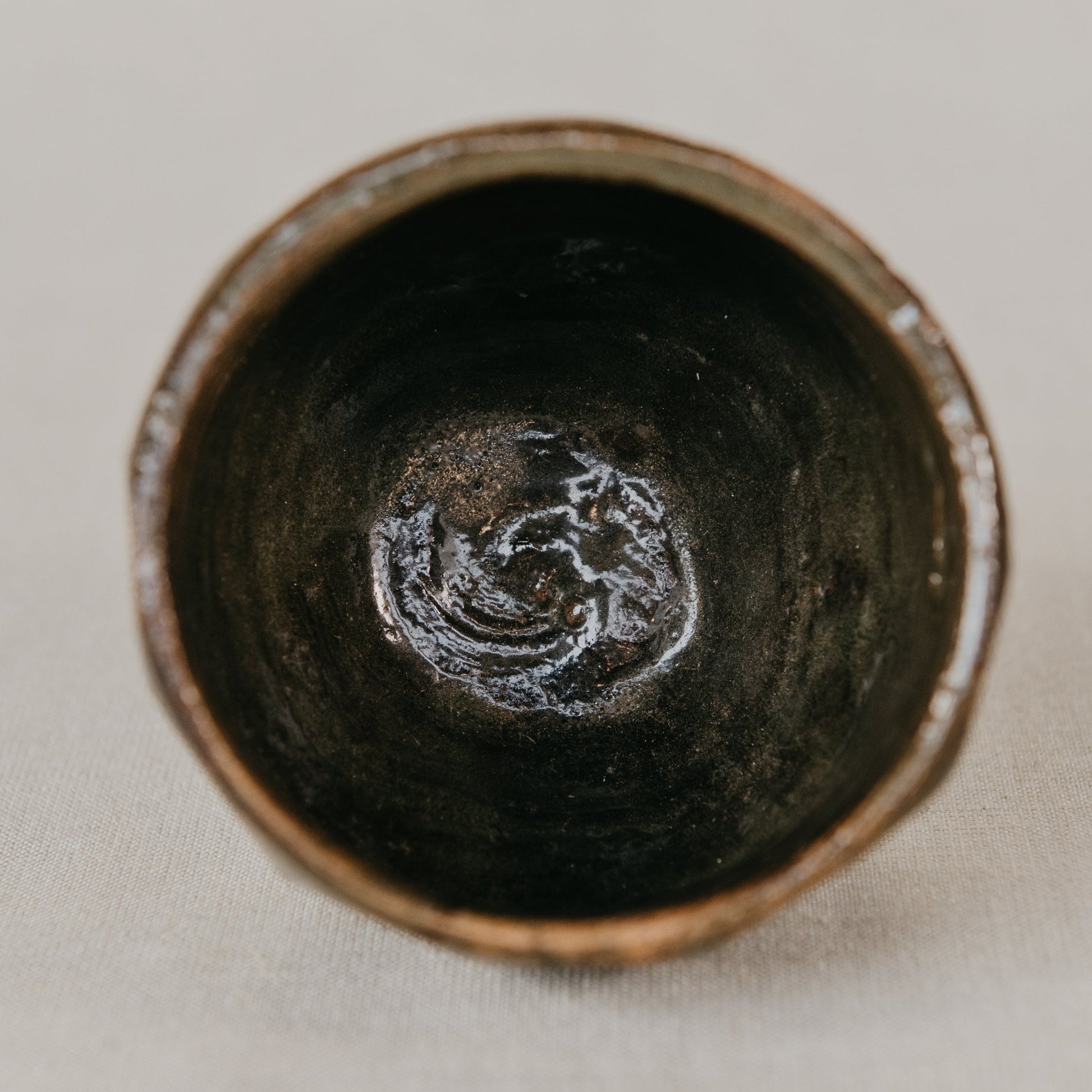 Close-up of a dark ceramic bowl with a textured interior on a light background
