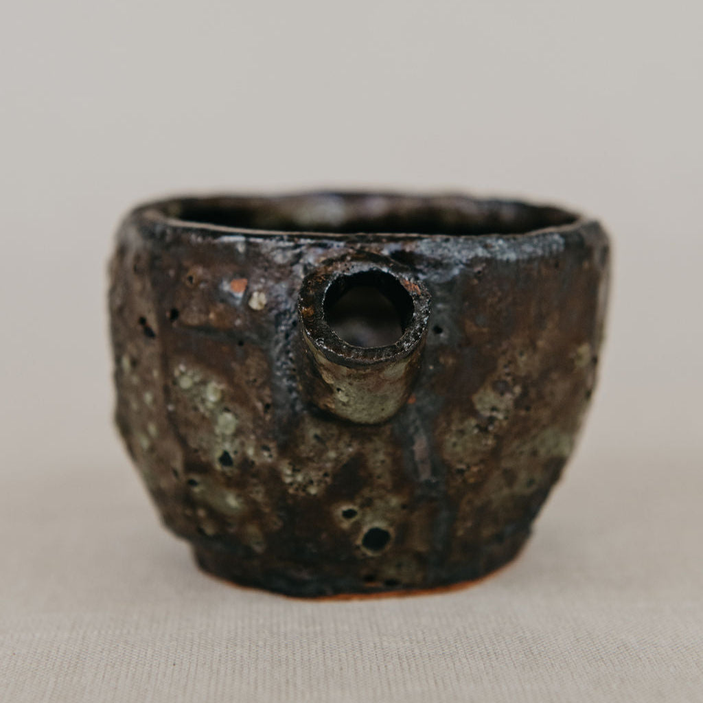 Rustic ceramic cup with textured surface on a beige background