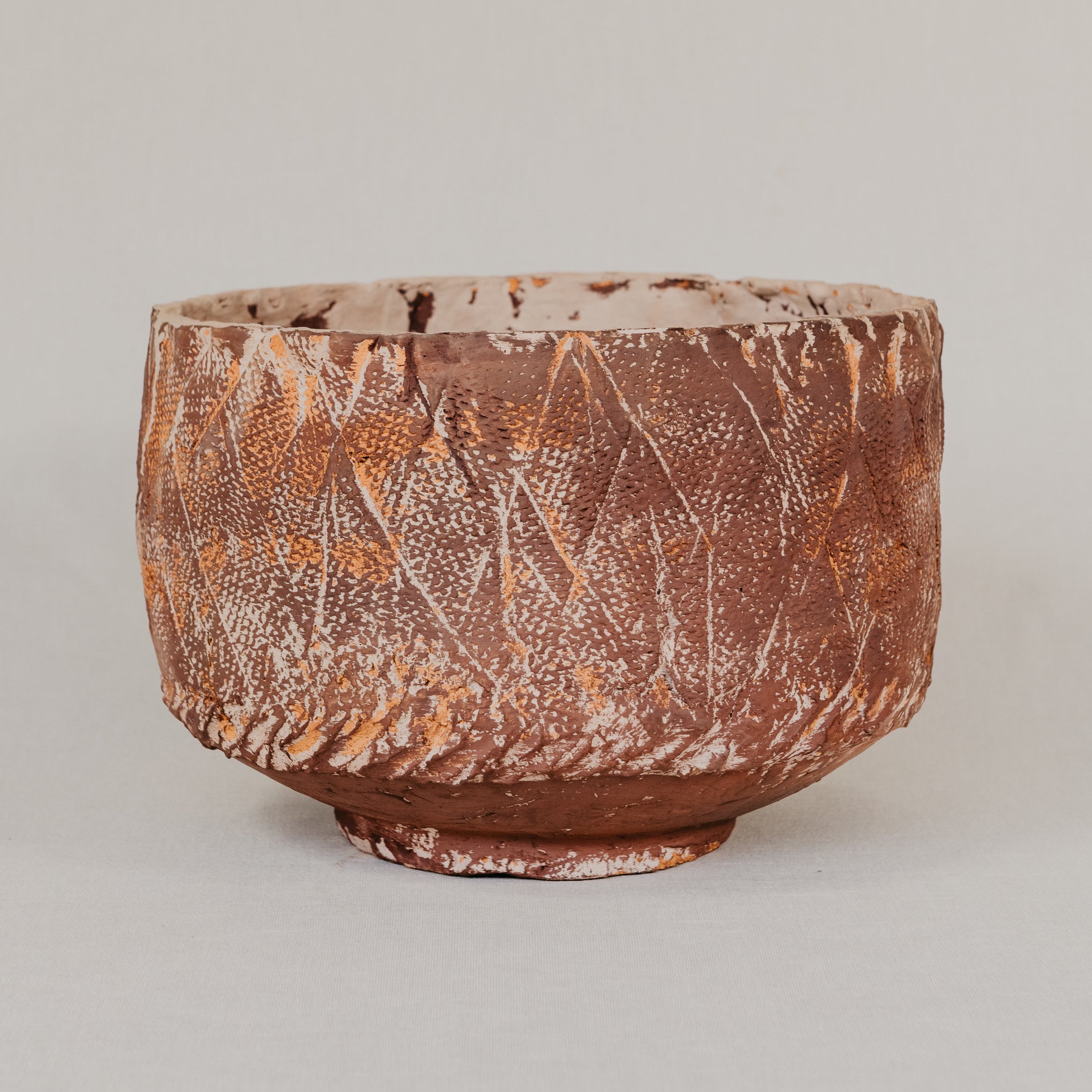 Brown ceramic pot with textured surface on a light gray background