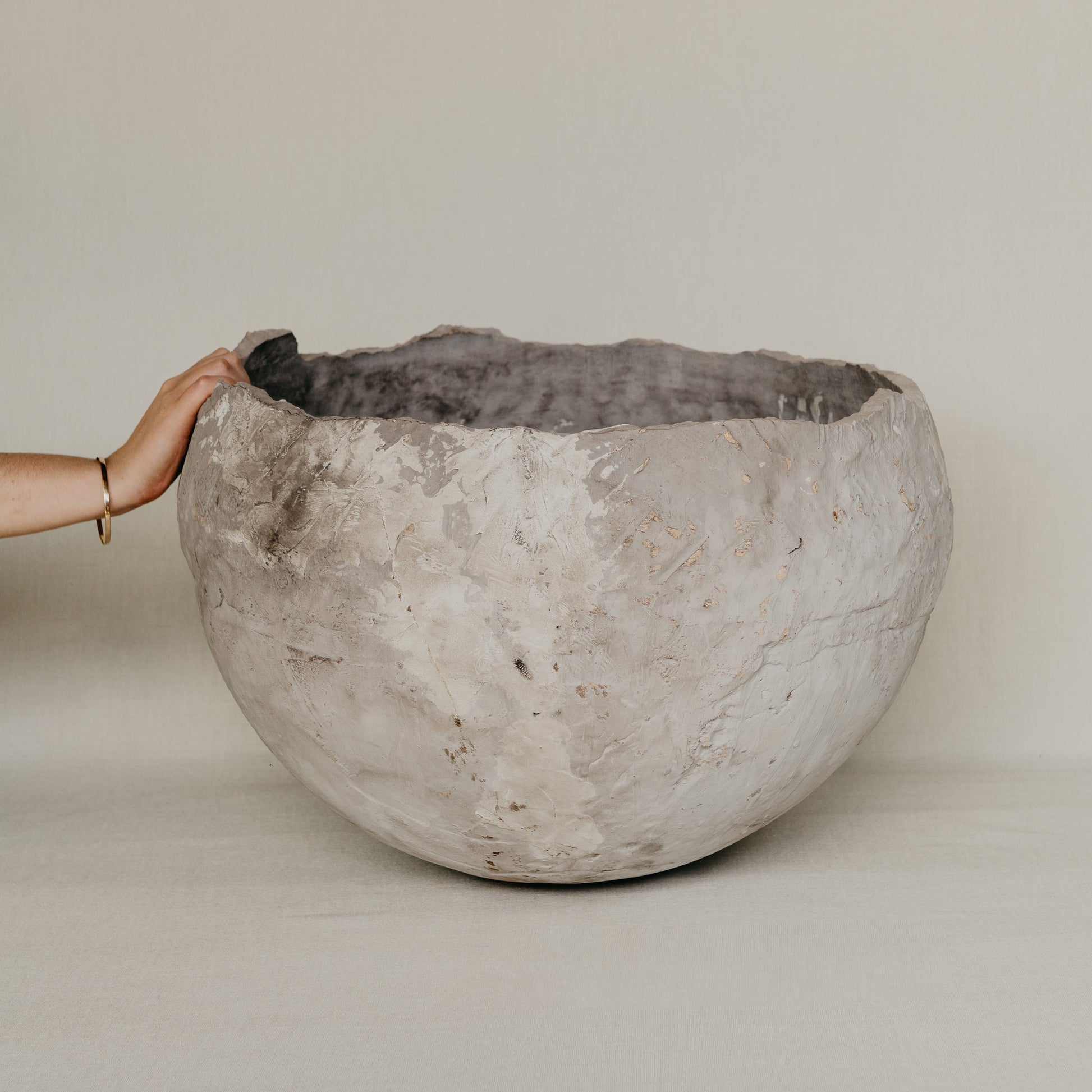 Large textured stone bowl held by a hand against a plain background