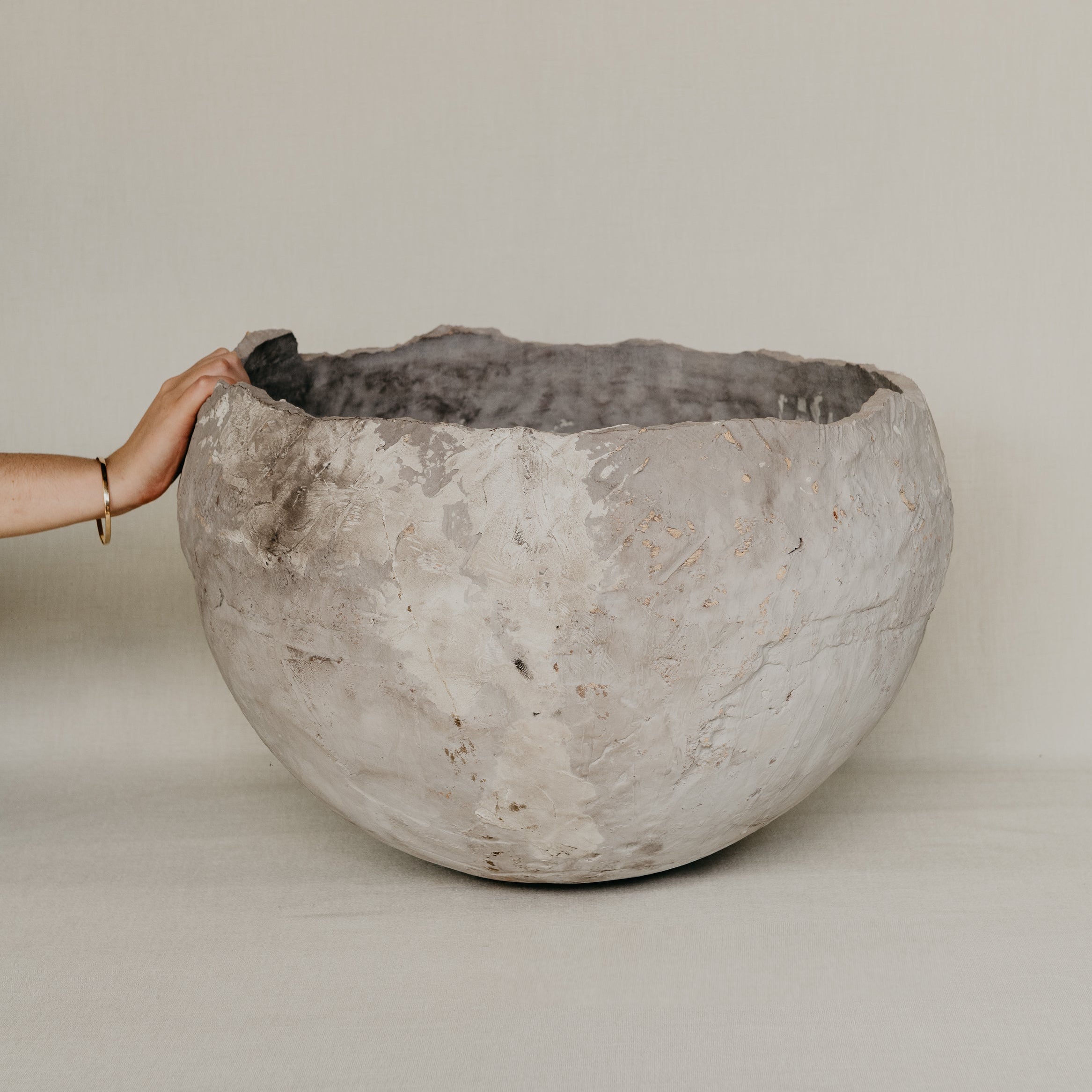 Large textured stone bowl held by a hand against a plain background