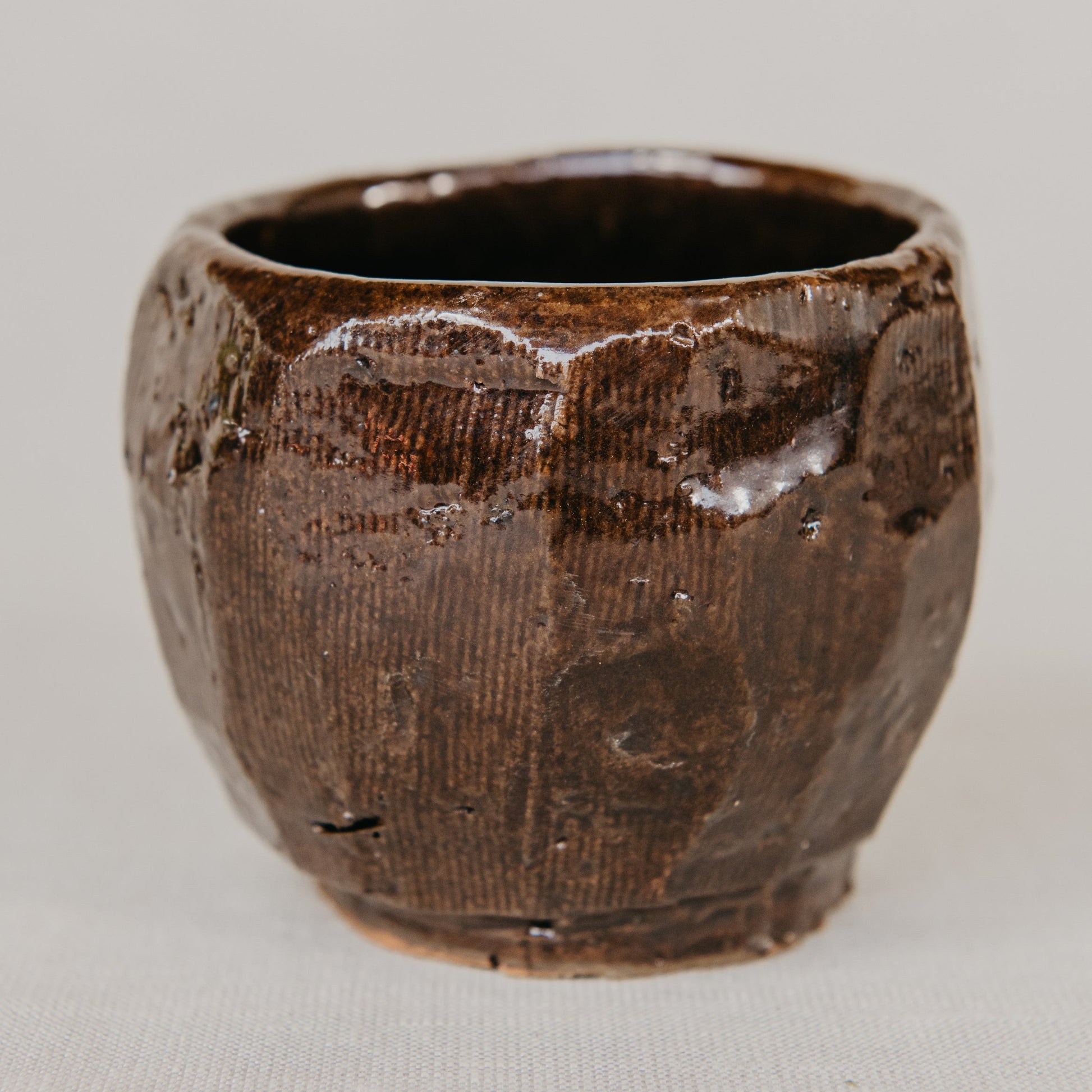 Brown ceramic cup with textured surface on a light gray background