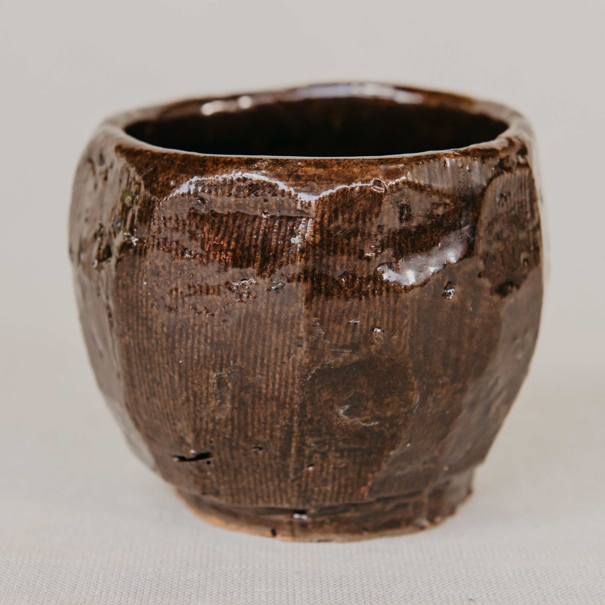 Brown ceramic cup with textured surface on a light gray background