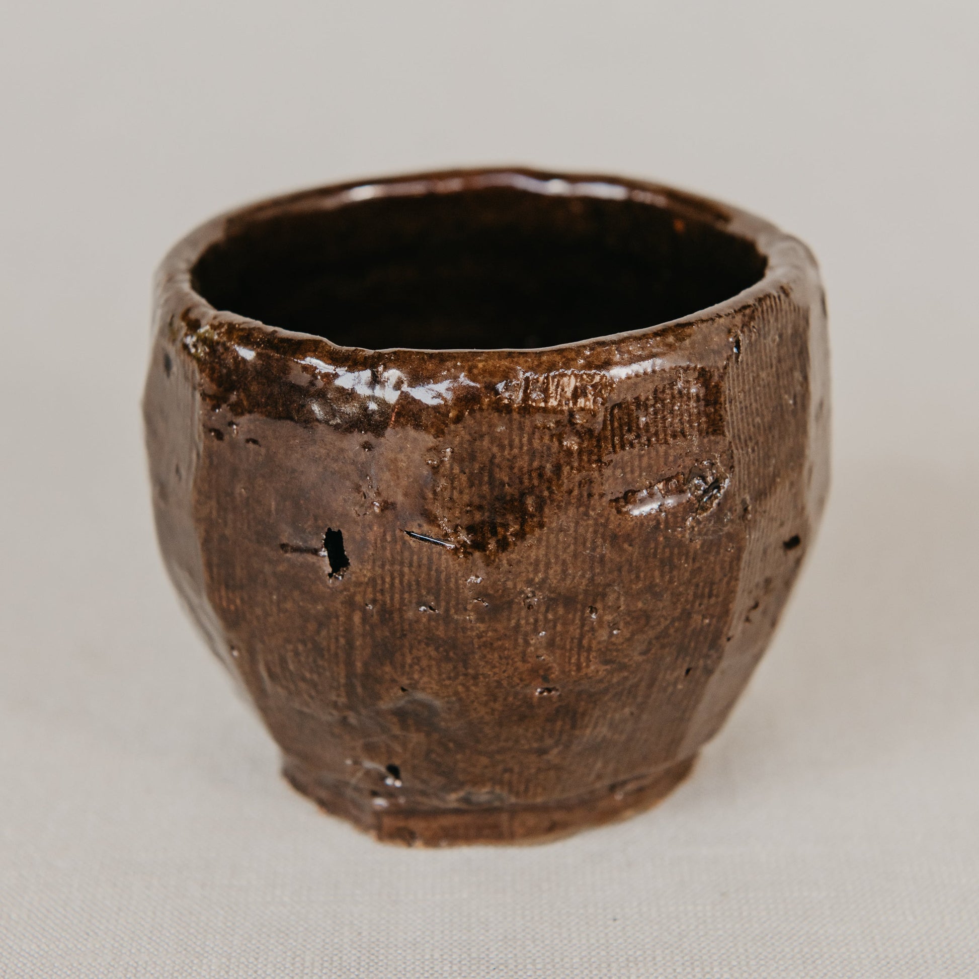 Brown ceramic cup with textured surface on a light gray background