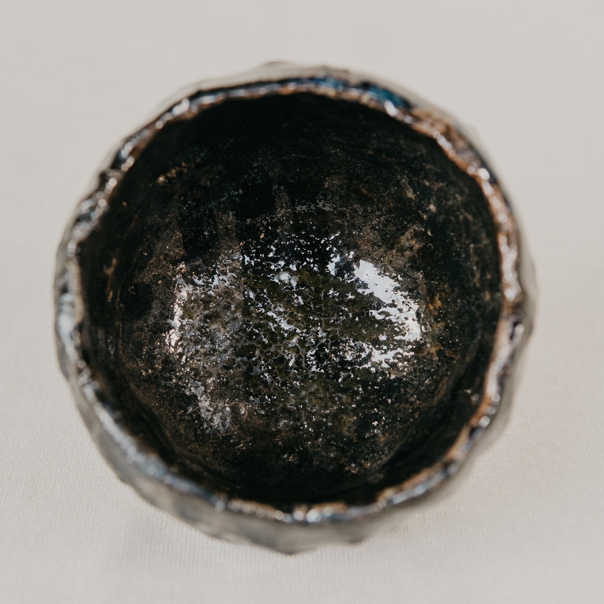 Close-up of a metallic object with a dark, possibly worn surface on a light gray background