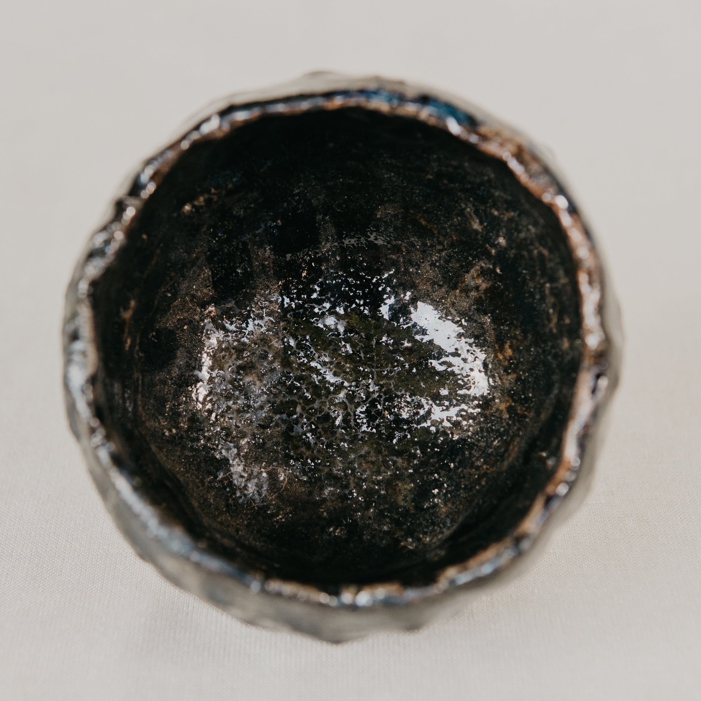 Close-up of a metallic object with a dark, possibly worn surface on a light gray background