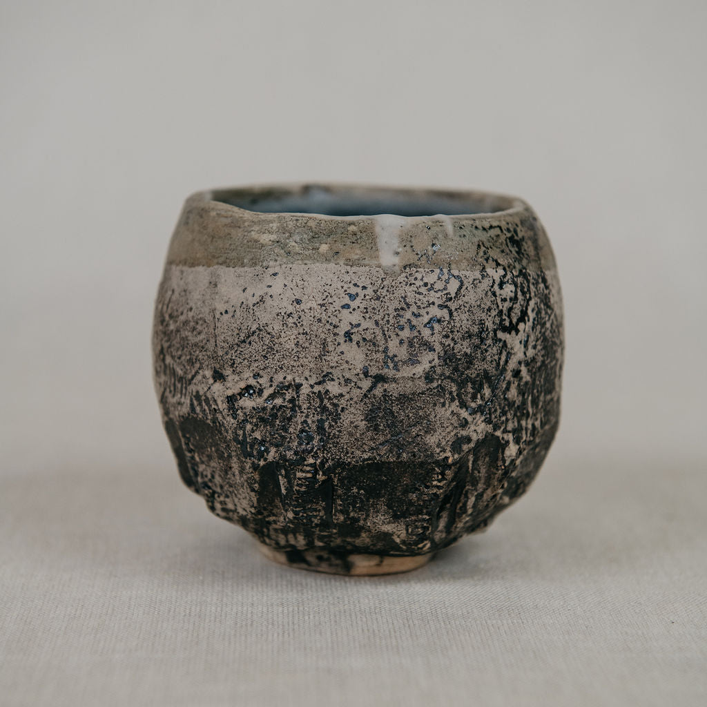 Small ceramic cup with textured surface on a plain background
