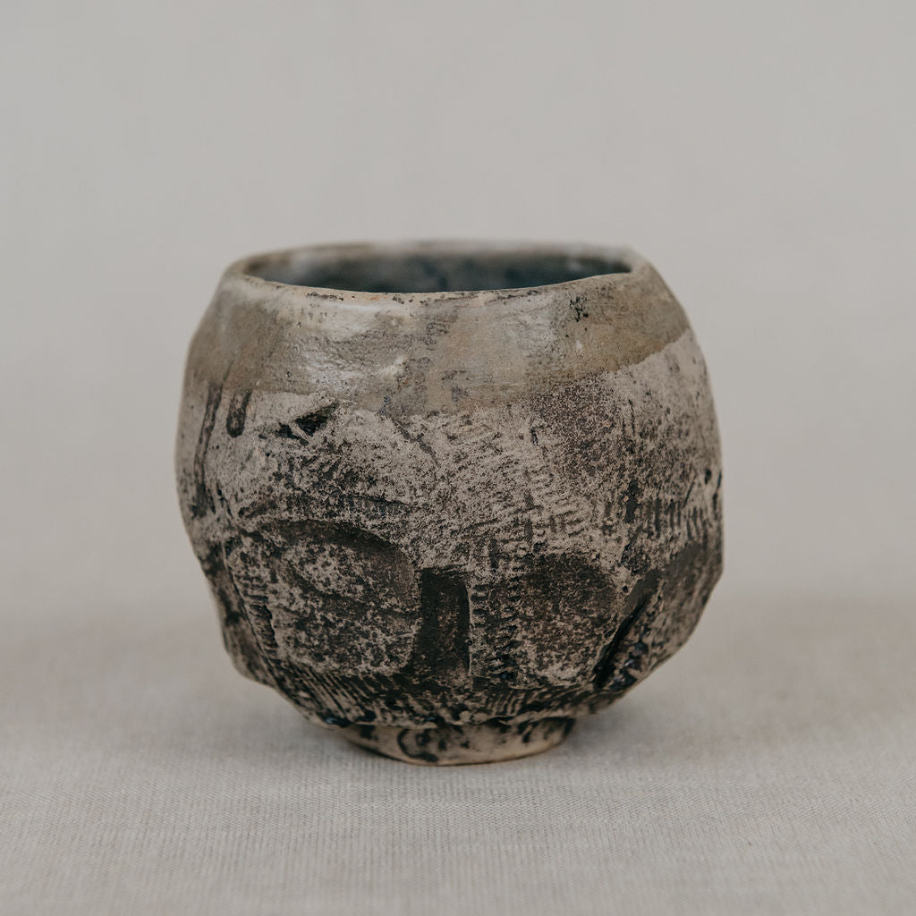 Small ceramic cup with textured surface on a plain background