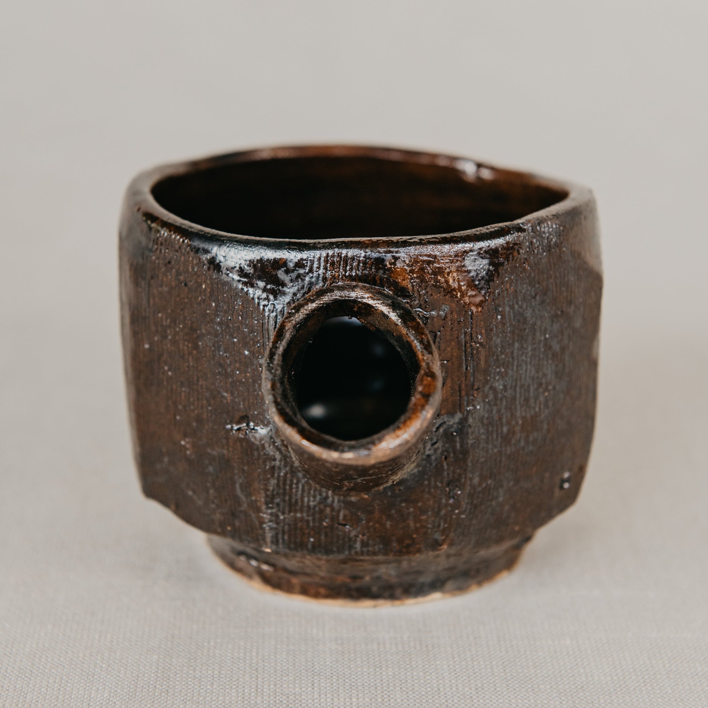 Brown ceramic cup with textured surface on a light gray background