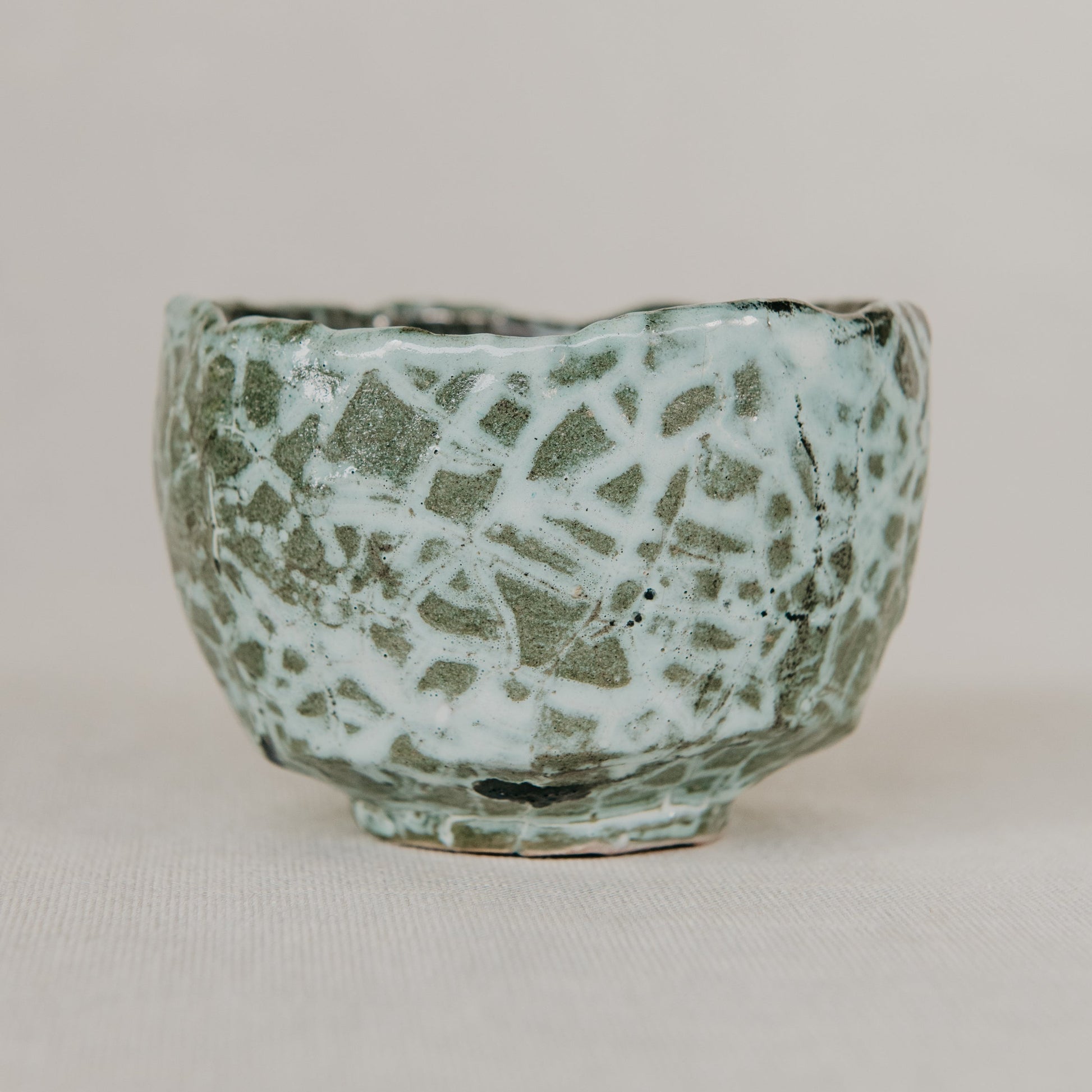 Green ceramic pot with textured surface on a beige background