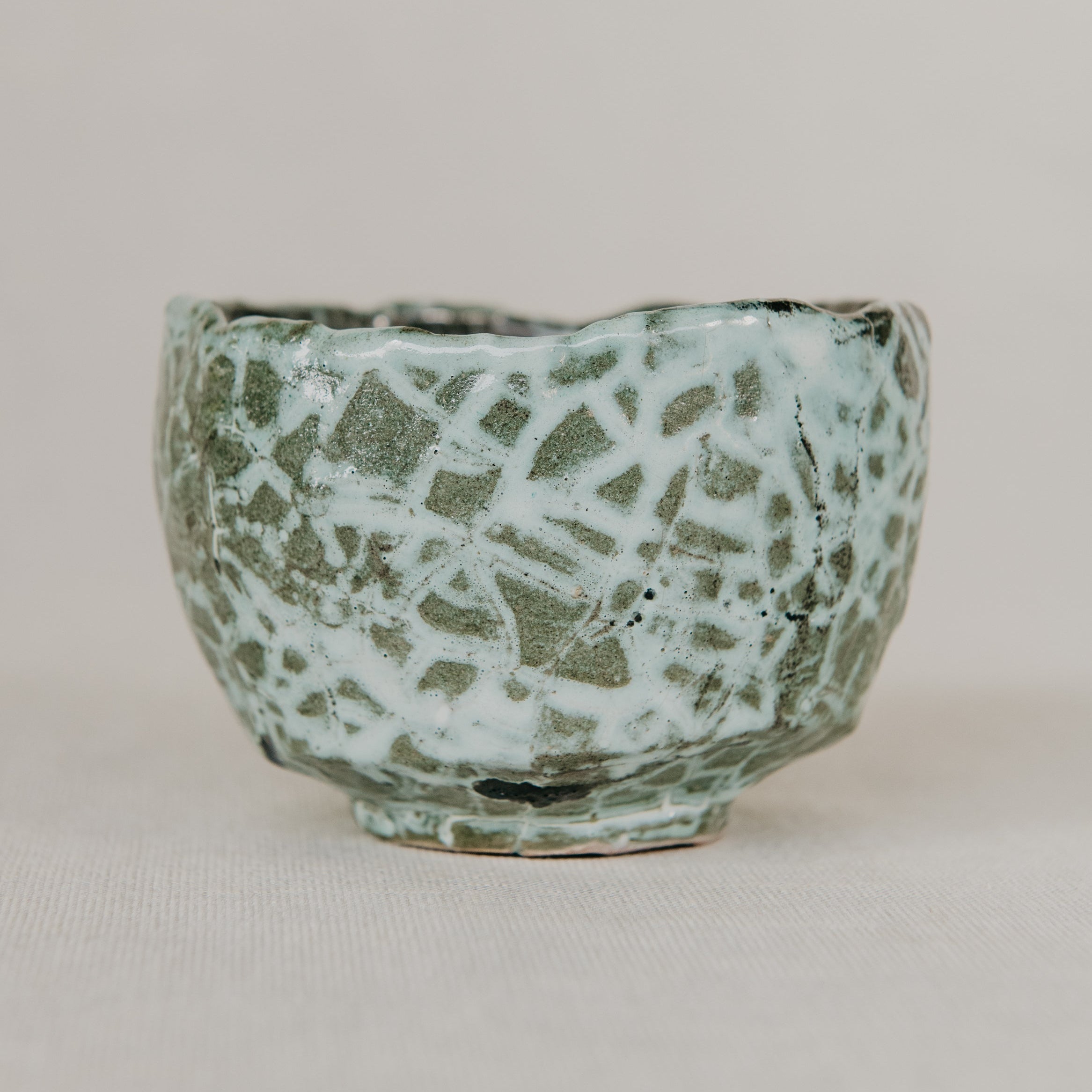 Green ceramic pot with textured surface on a beige background