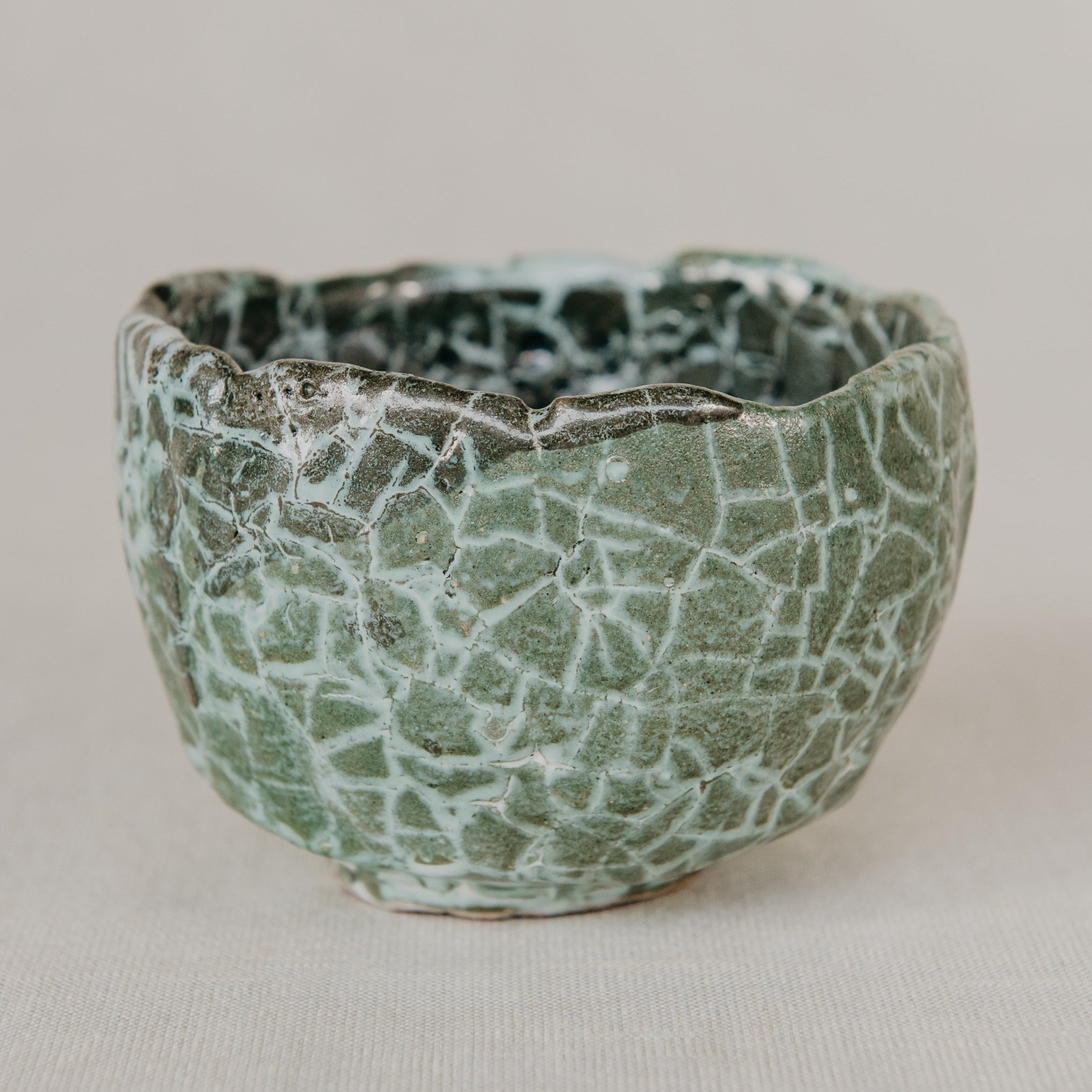 Ceramic bowl with a textured green and black surface on a beige background