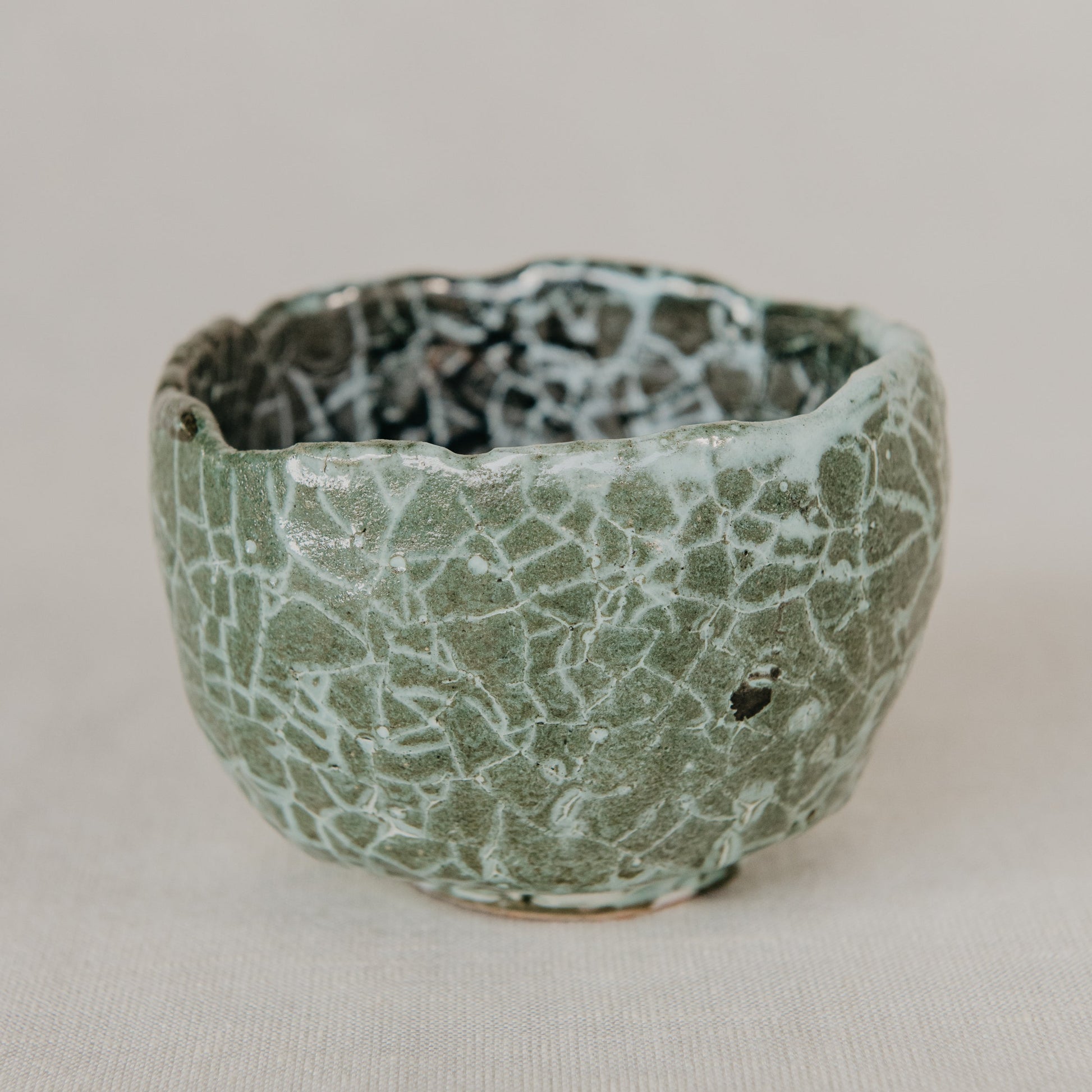 Small ceramic bowl with textured green and black surface on a beige background