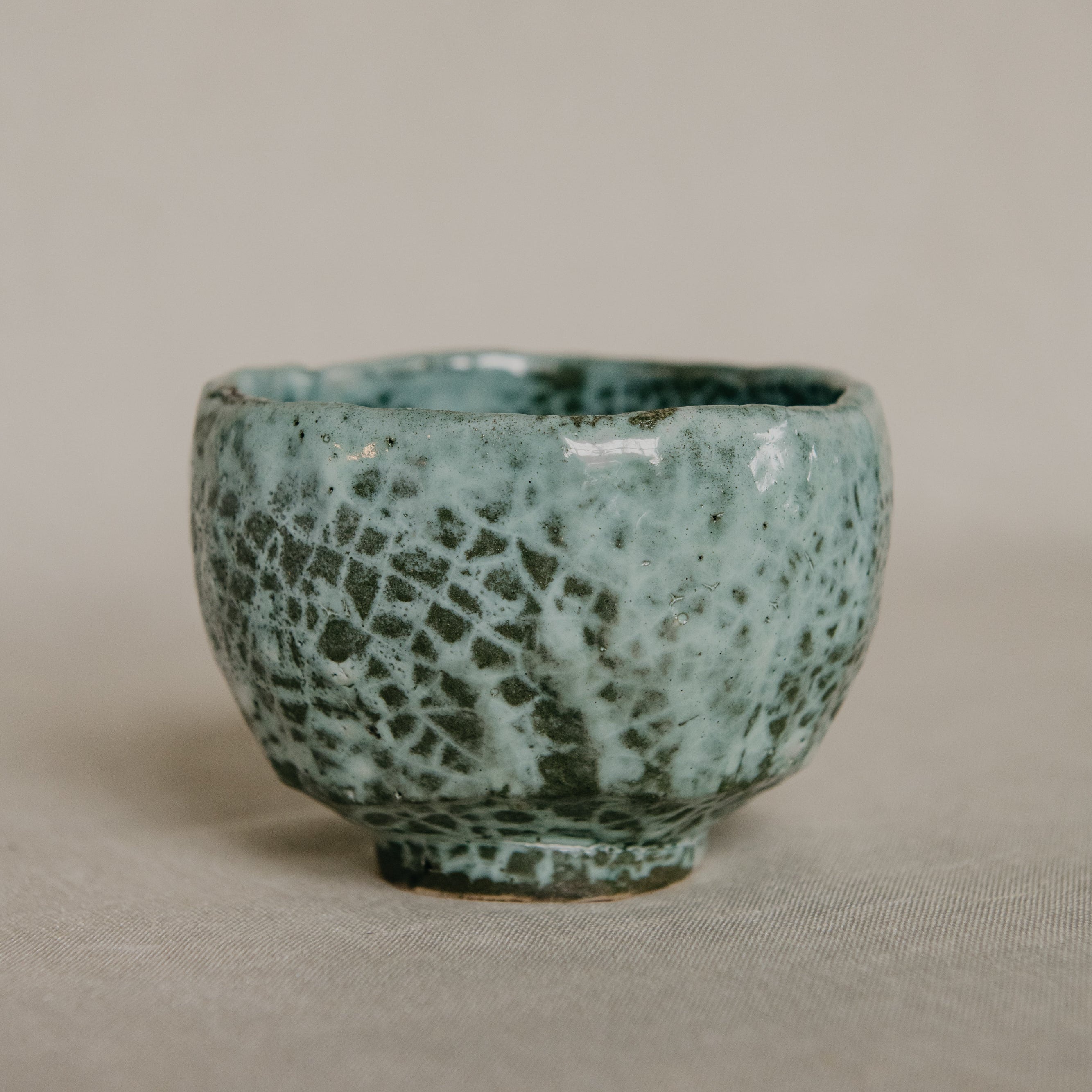 Green ceramic cup with textured surface on a beige background