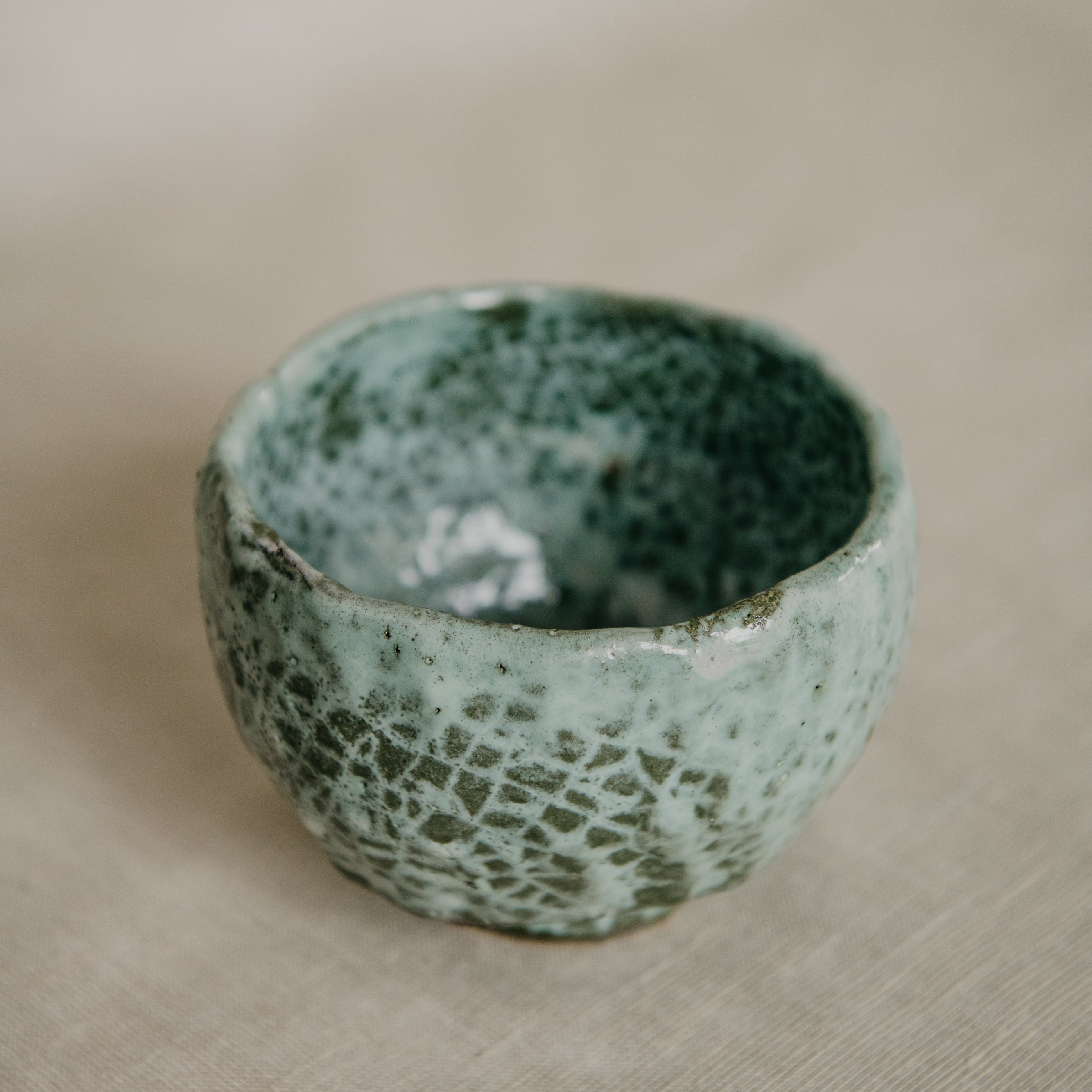 Green ceramic bowl with textured surface on a beige fabric background