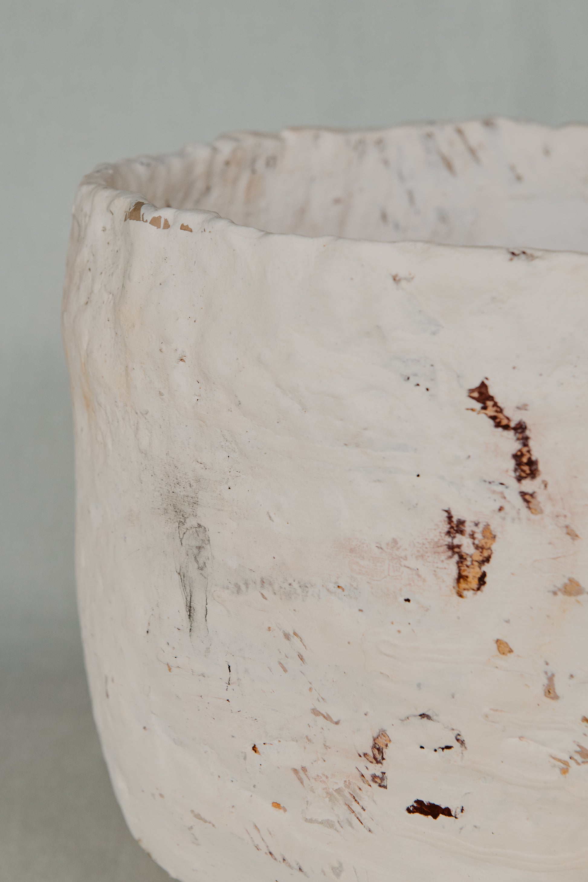 Close-up of a textured white ceramic vase with brown specks on a light gray background