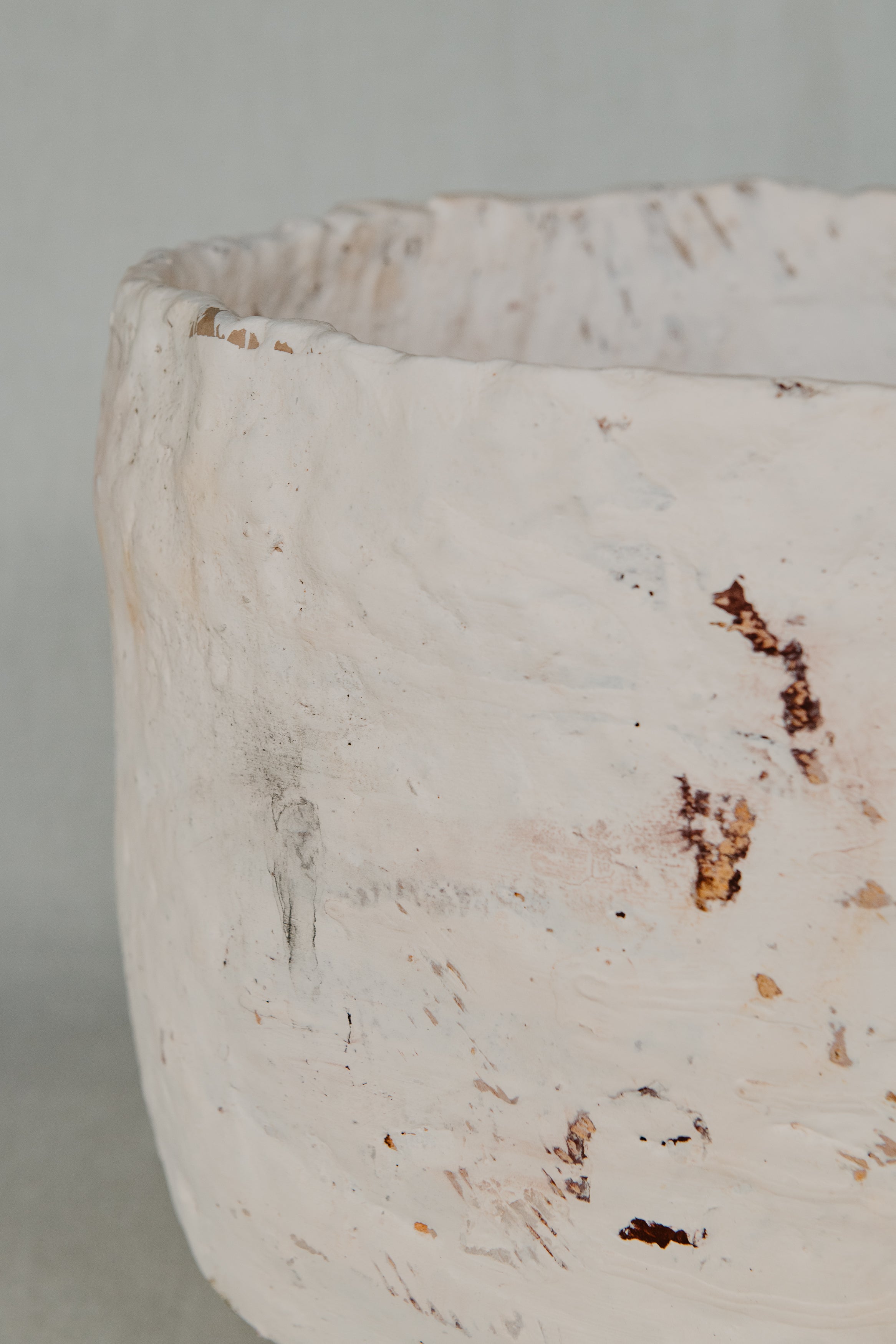 Close-up of a textured white ceramic vase with brown specks on a light gray background