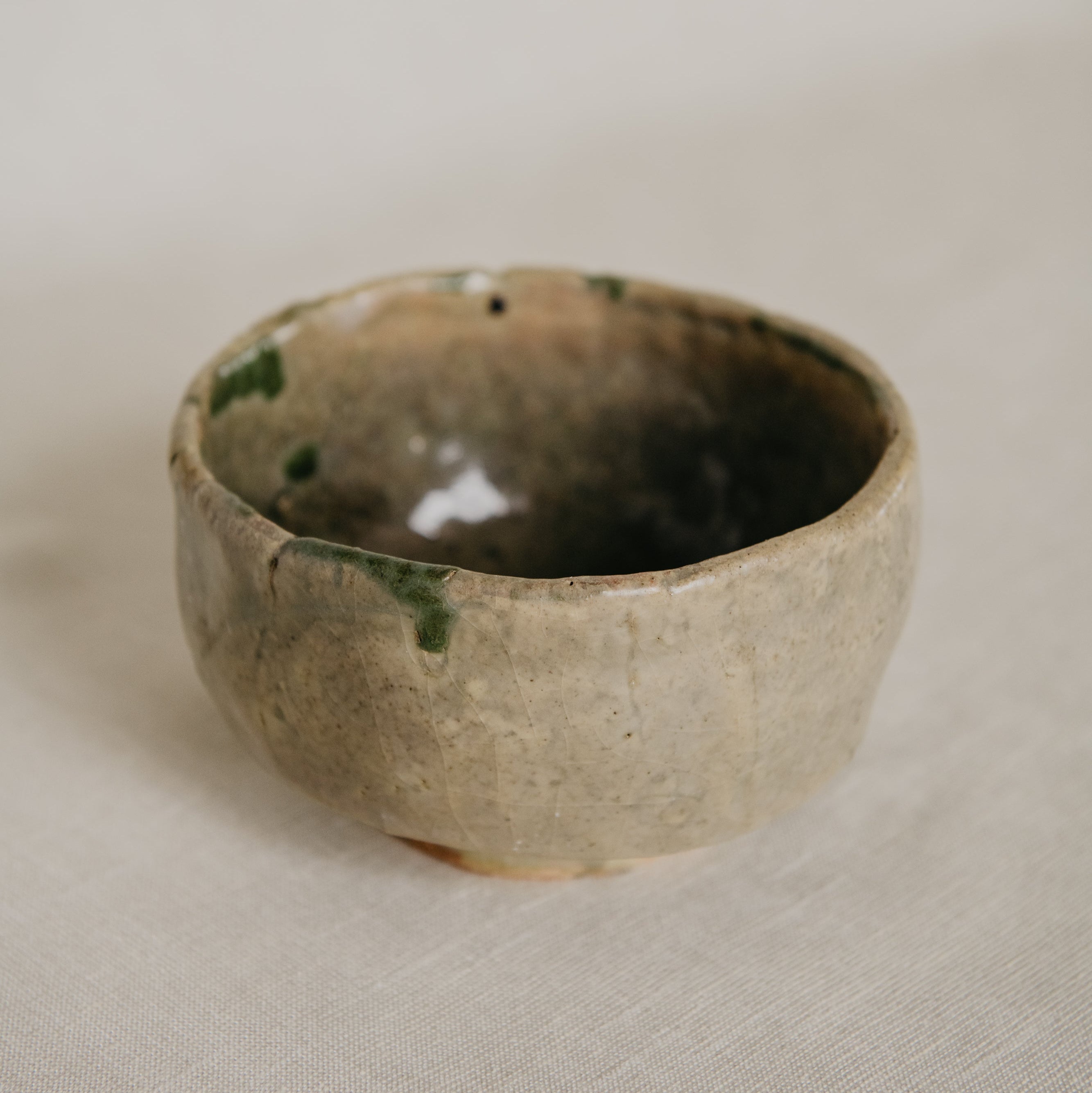 Small ceramic bowl with green and black speckles on a beige background